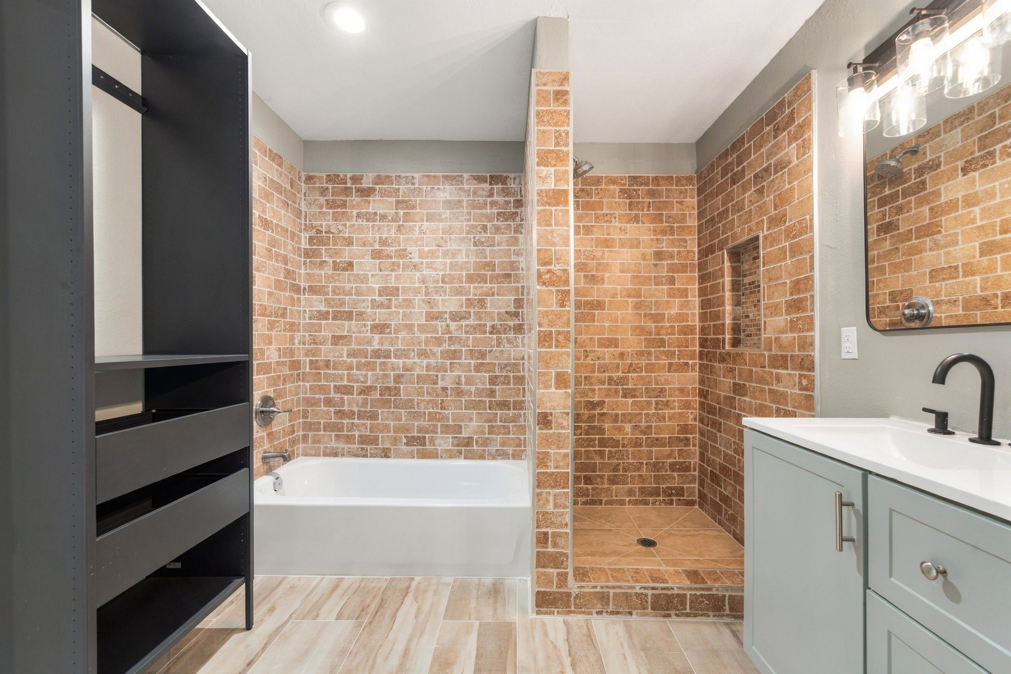 Elegant bathroom featuring a spacious walk-in shower with rustic brick tiles, a modern bathtub, sleek vanity with a black faucet, and ample storage space.