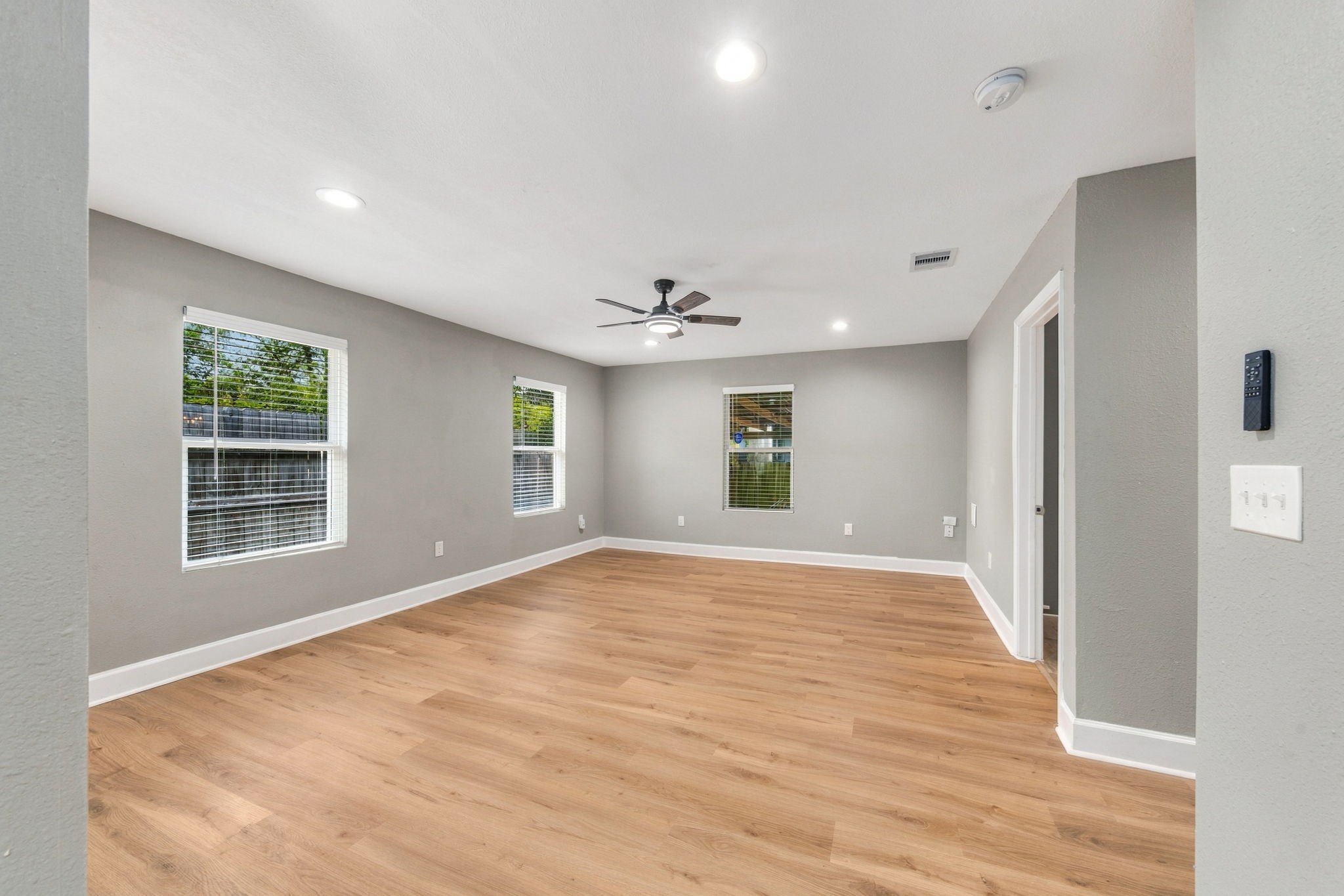 Spacious living area featuring sleek hardwood floors, modern gray walls, and ample natural light from multiple windows.