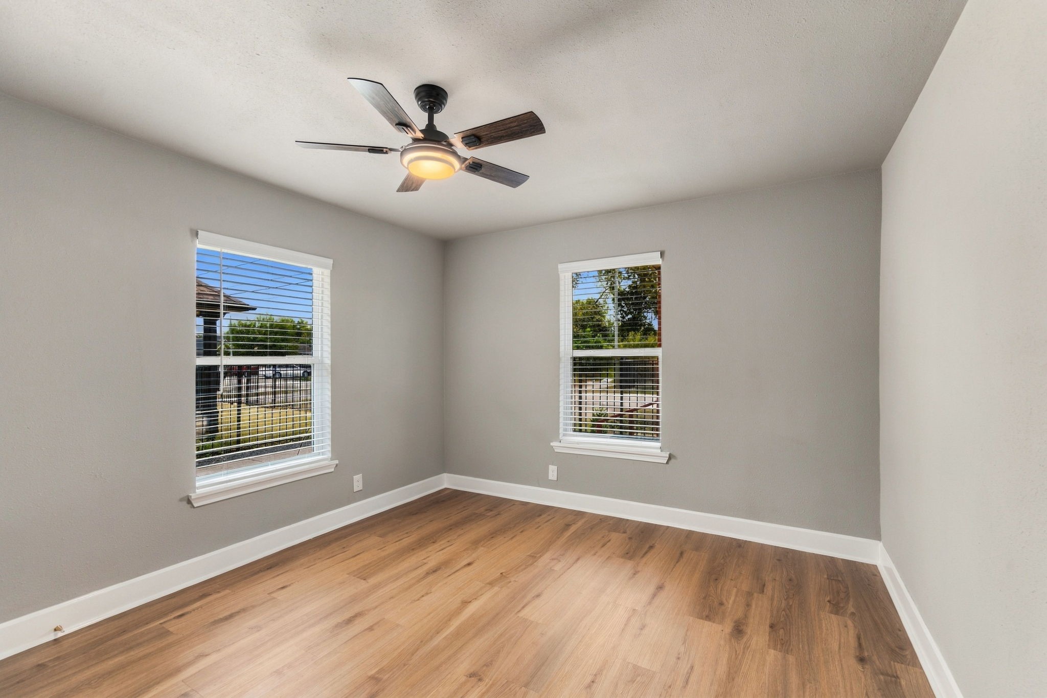 Bright and inviting room with large windows, modern ceiling fan, and beautiful hardwood floors.