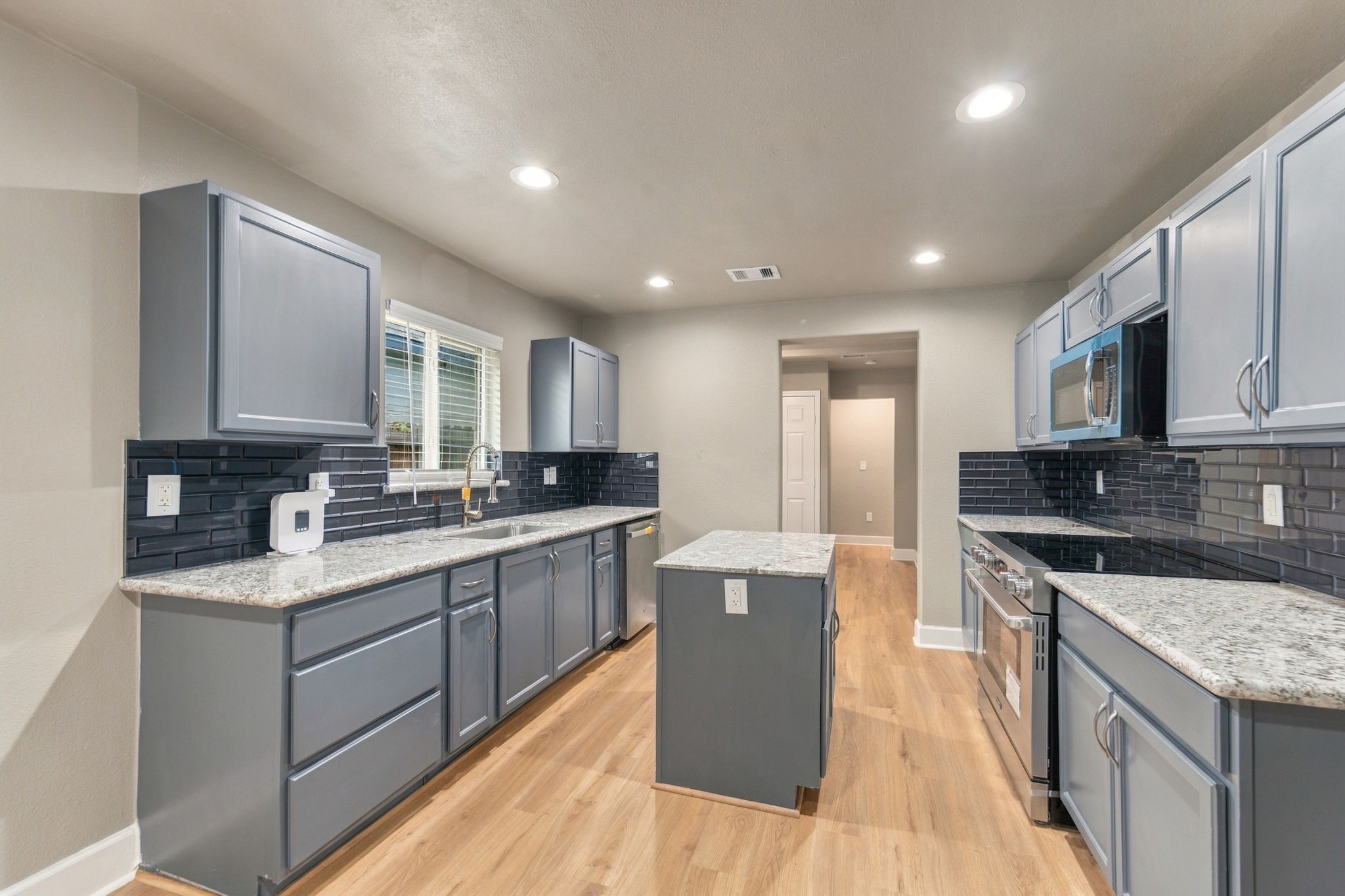 Modern kitchen with sleek gray cabinets, granite countertops, and a stylish subway tile backsplash, complemented by stainless steel appliances and recessed lighting.