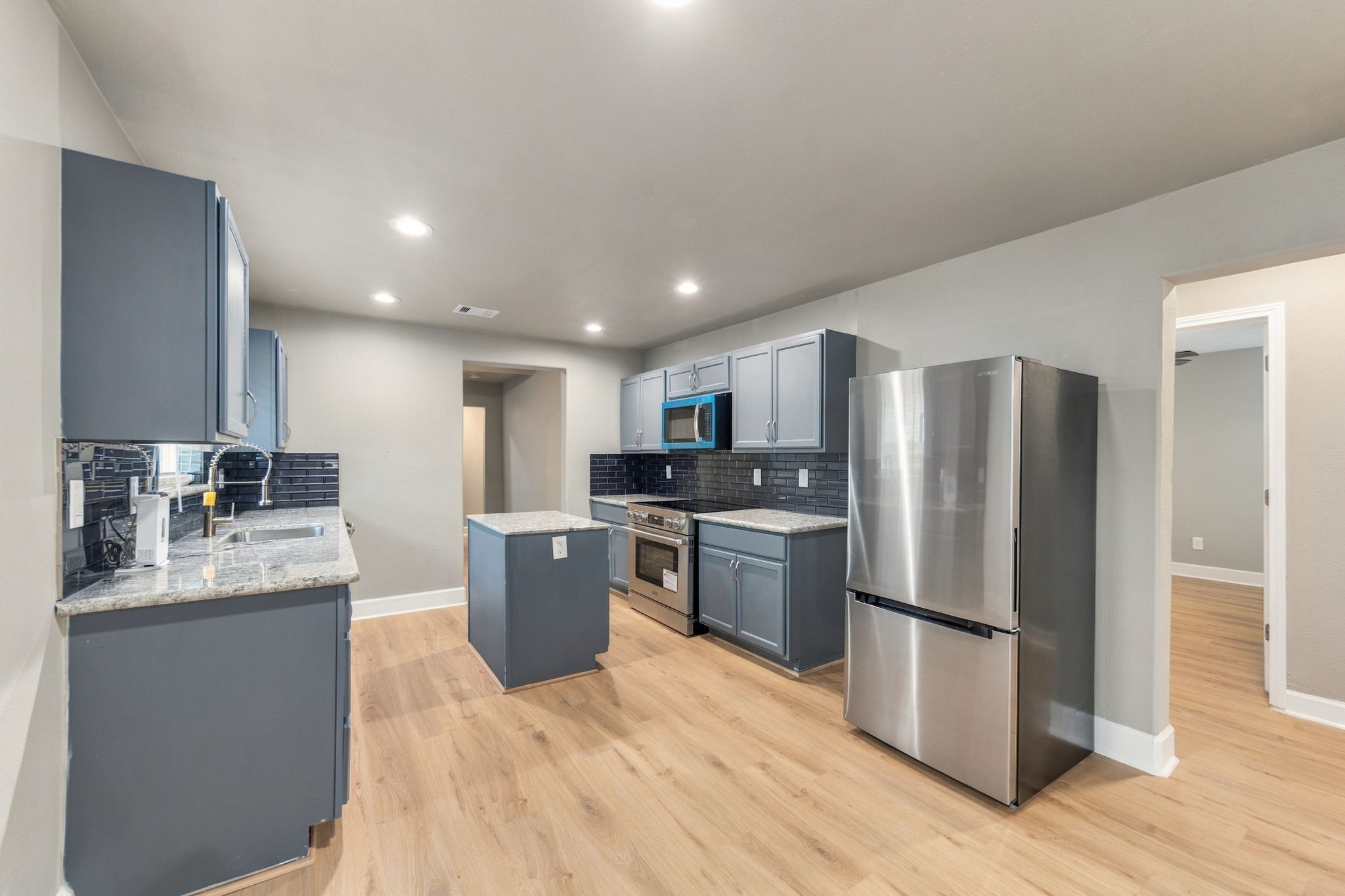 Modern kitchen featuring sleek stainless steel appliances, elegant gray cabinetry, and a stylish dark backsplash.