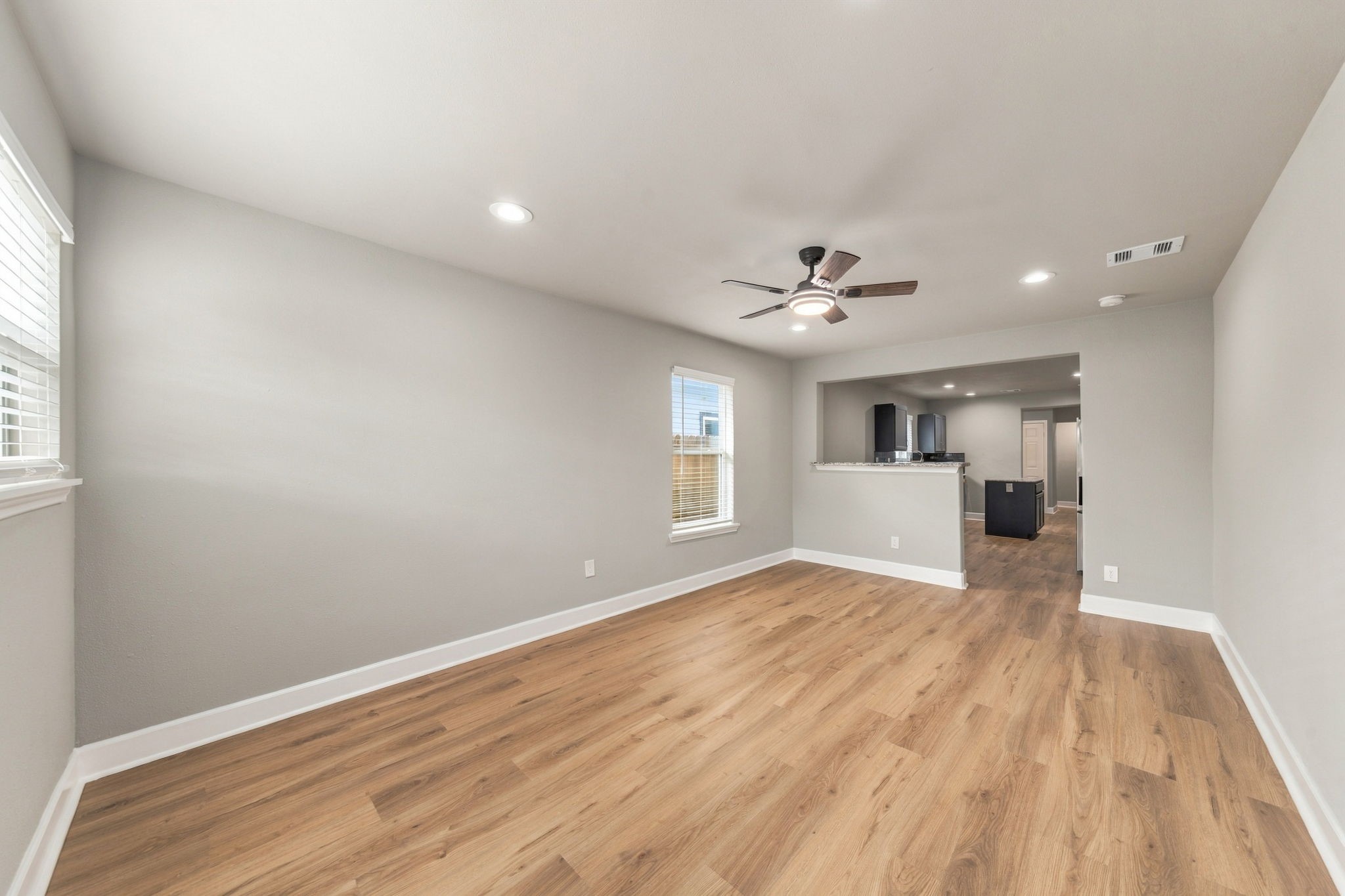 Bright and spacious living area with hardwood floors, modern ceiling fan, and recessed lighting, seamlessly connected to the kitchen for easy entertaining.