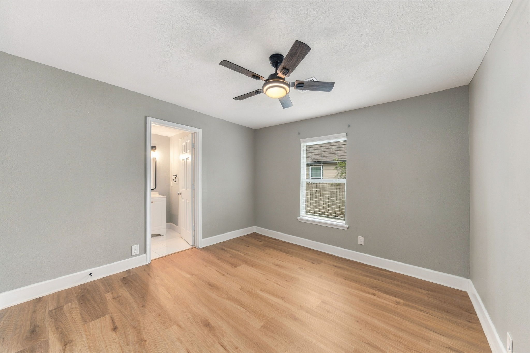 Spacious bedroom featuring fresh neutral paint, sleek hardwood flooring, and a ceiling fan, with an en-suite bathroom for added convenience.