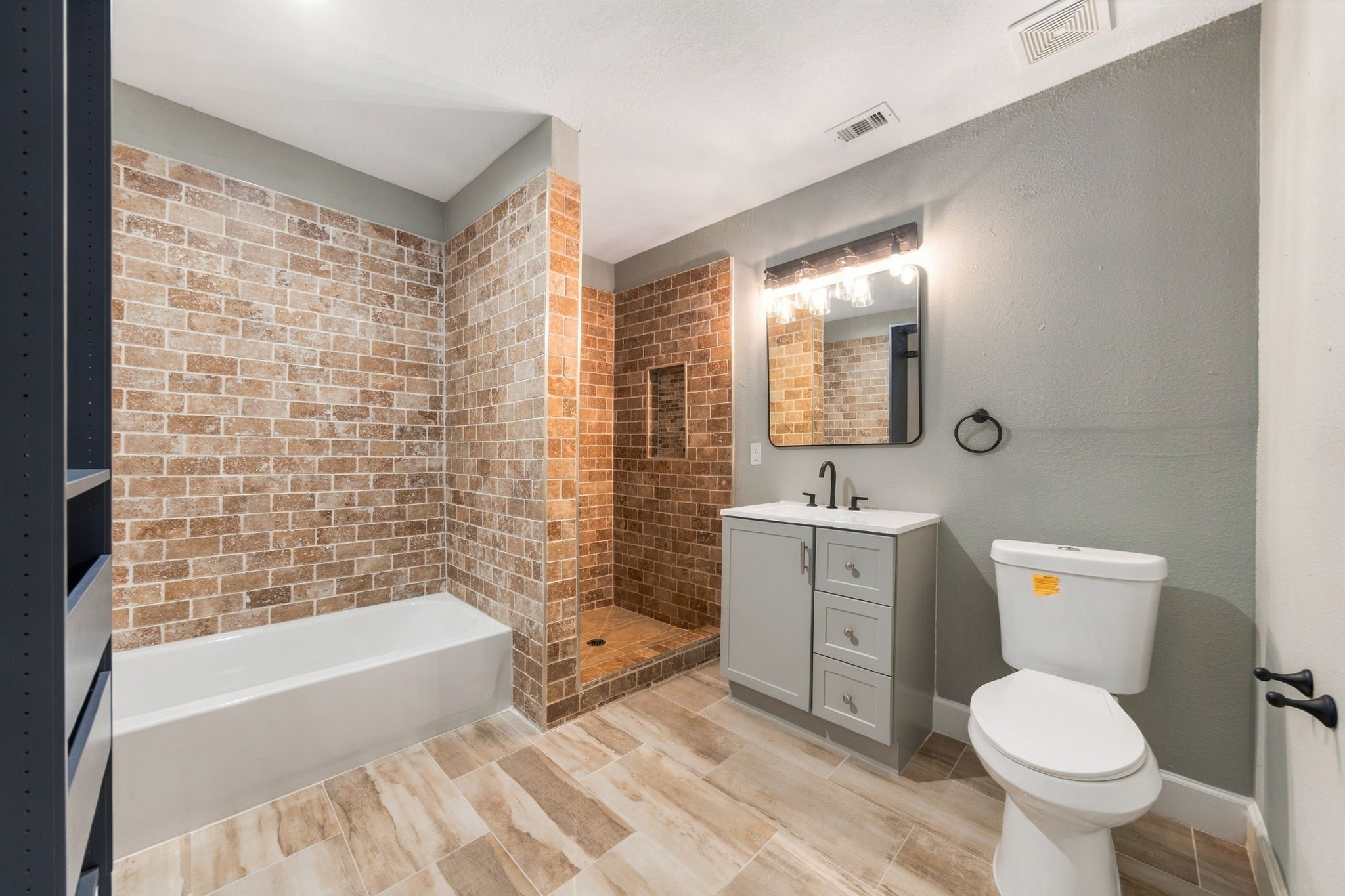 Spacious bathroom featuring a modern vanity, stylish brick tile shower, and a separate bathtub, all complemented by elegant lighting and neutral tones.