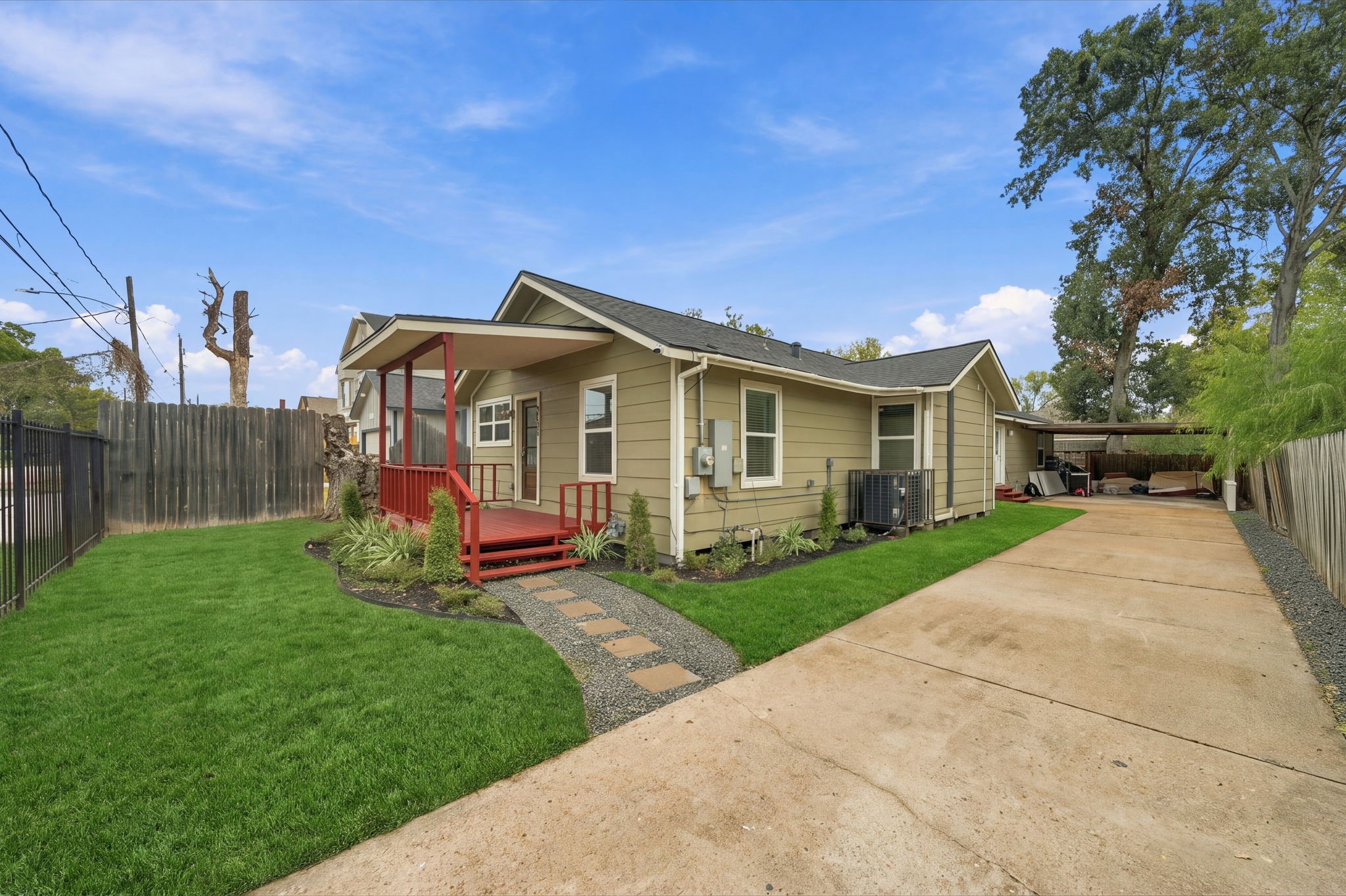 Charming single-story home with a welcoming red front porch, manicured lawn, and long driveway leading to a covered parking area.