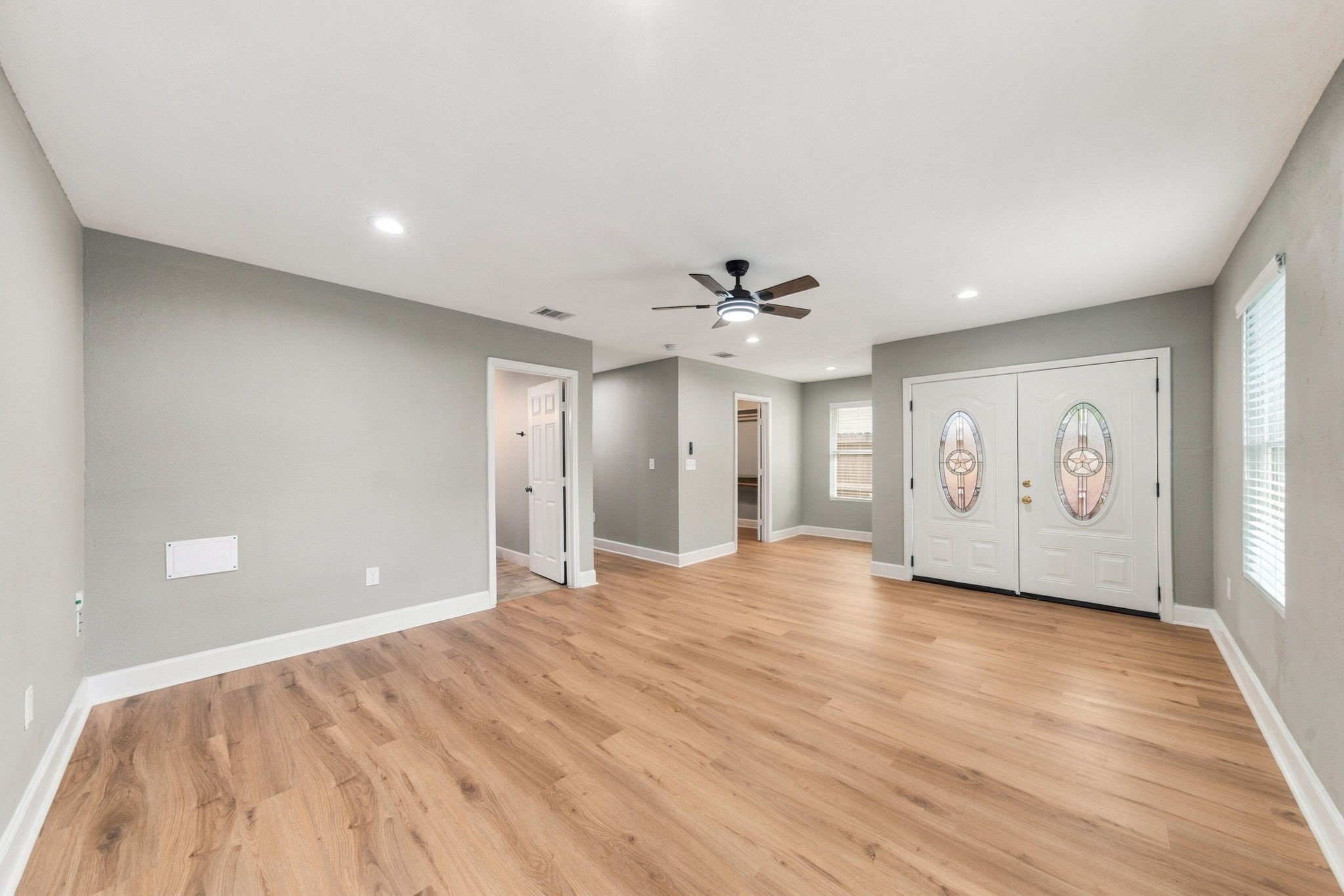 Spacious living area with warm wood flooring, modern ceiling fan, and elegant double doors, offering a welcoming and stylish entrance.