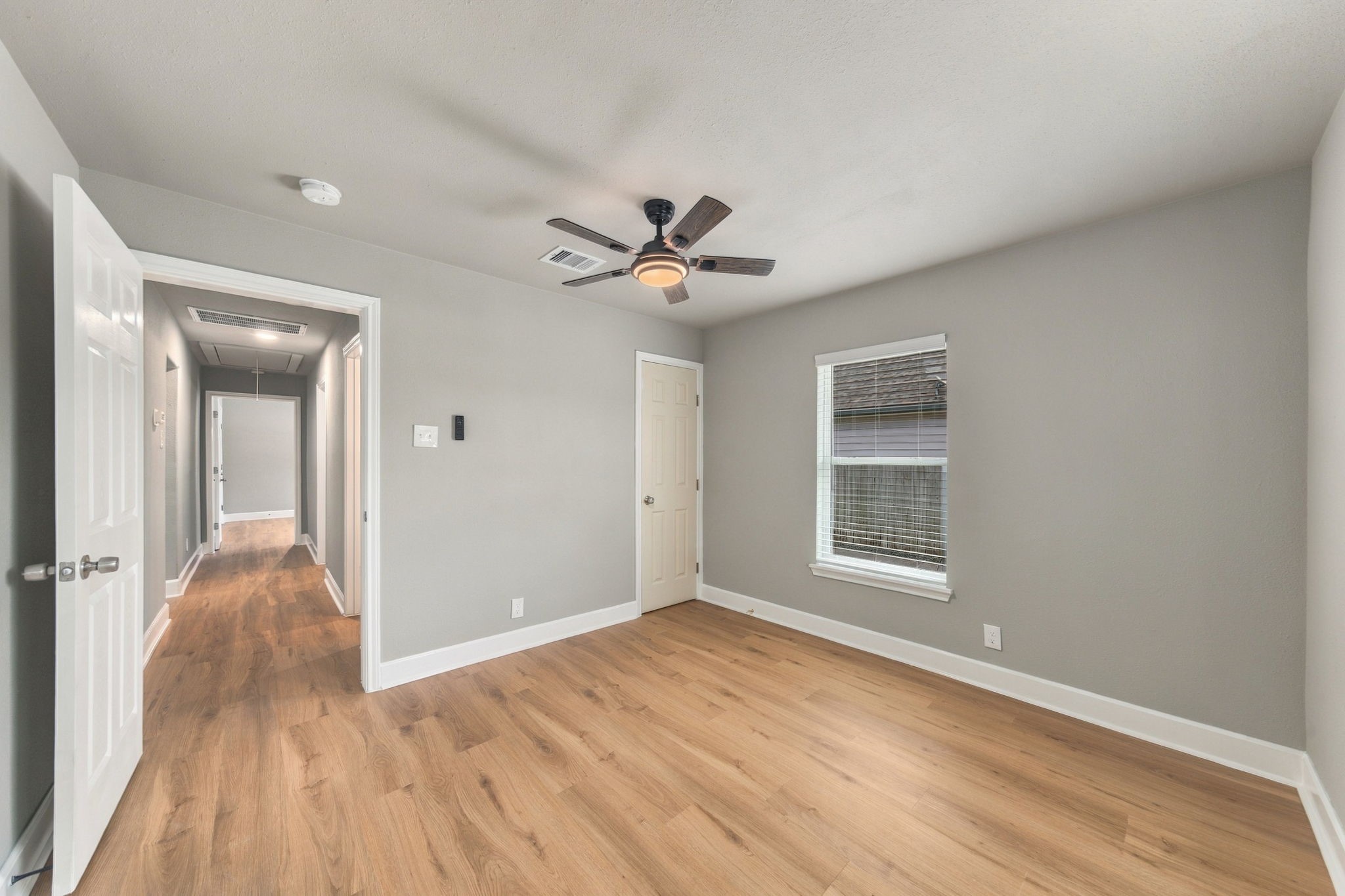 Spacious bedroom with hardwood floors, neutral walls, and a ceiling fan, offering ample natural light through a large window.