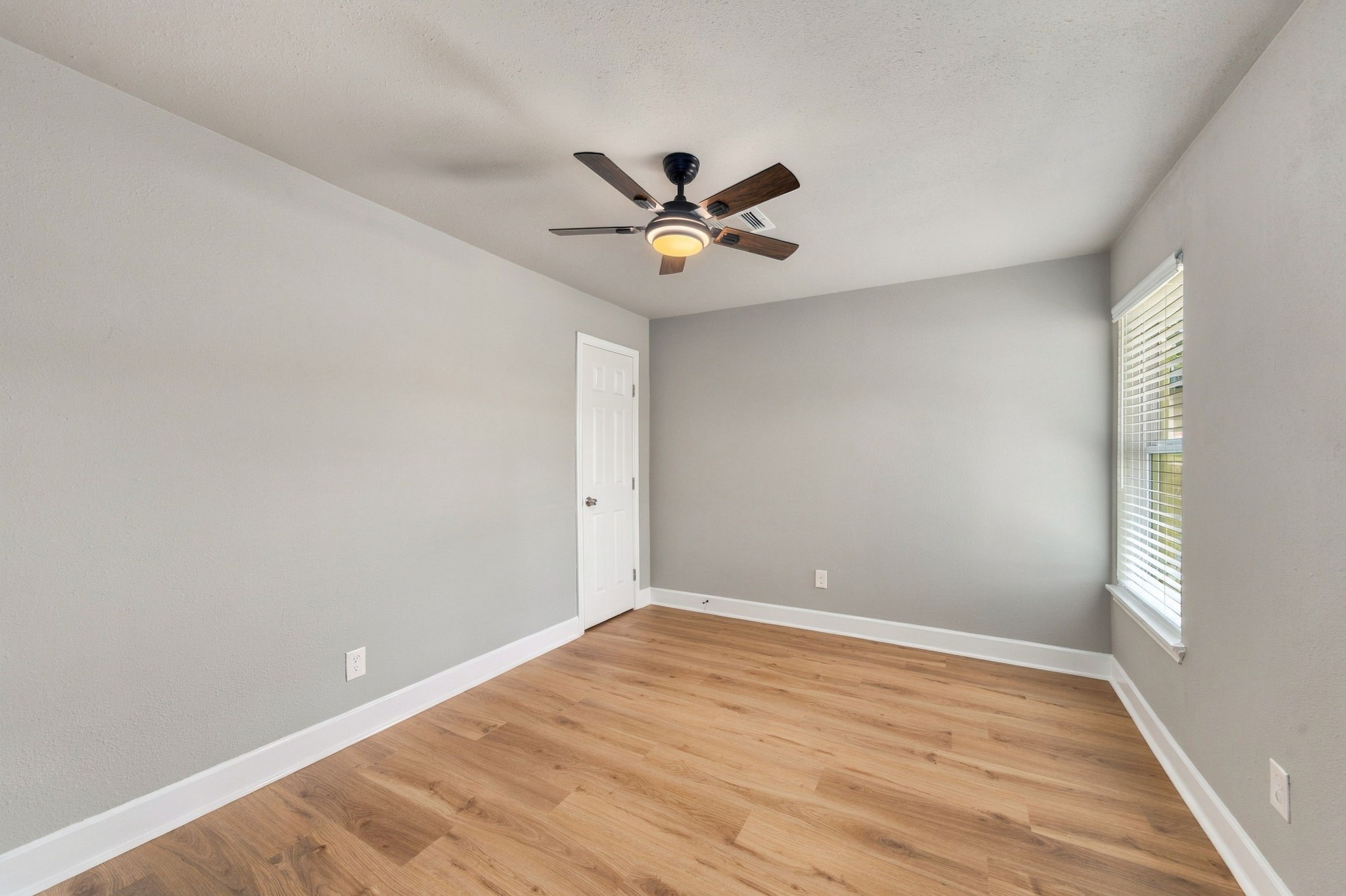 Bright and inviting room featuring sleek hardwood floors, a modern ceiling fan, and abundant natural light through large windows.