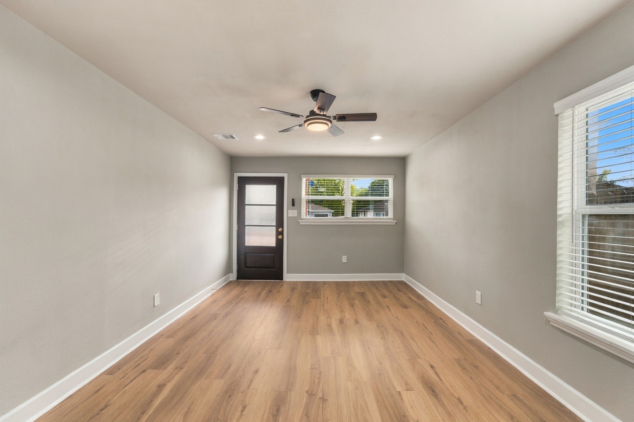 Bright and inviting room with wood flooring, complemented by a modern ceiling fan and ample natural light from multiple windows.