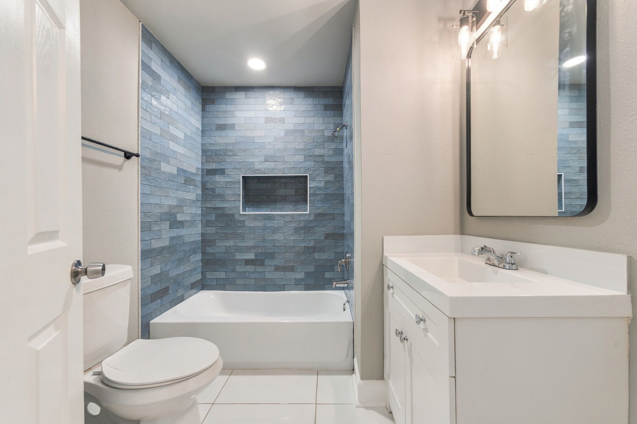 Sleek bathroom featuring a stylish blue tiled shower, modern vanity with ample storage, and elegant lighting.