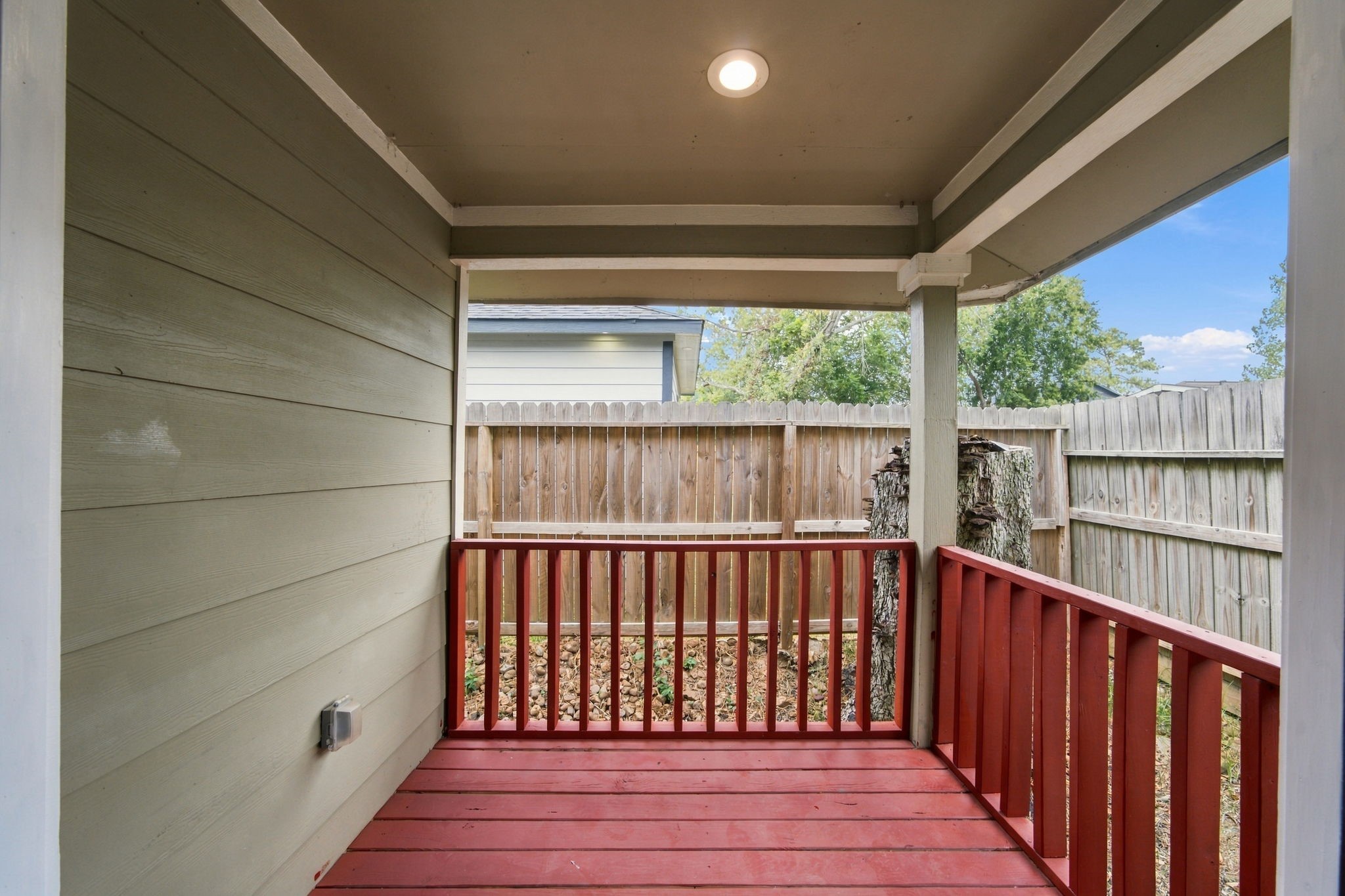Charming covered patio with vibrant red railing offers a cozy outdoor space, perfect for relaxing and enjoying the fresh air.
