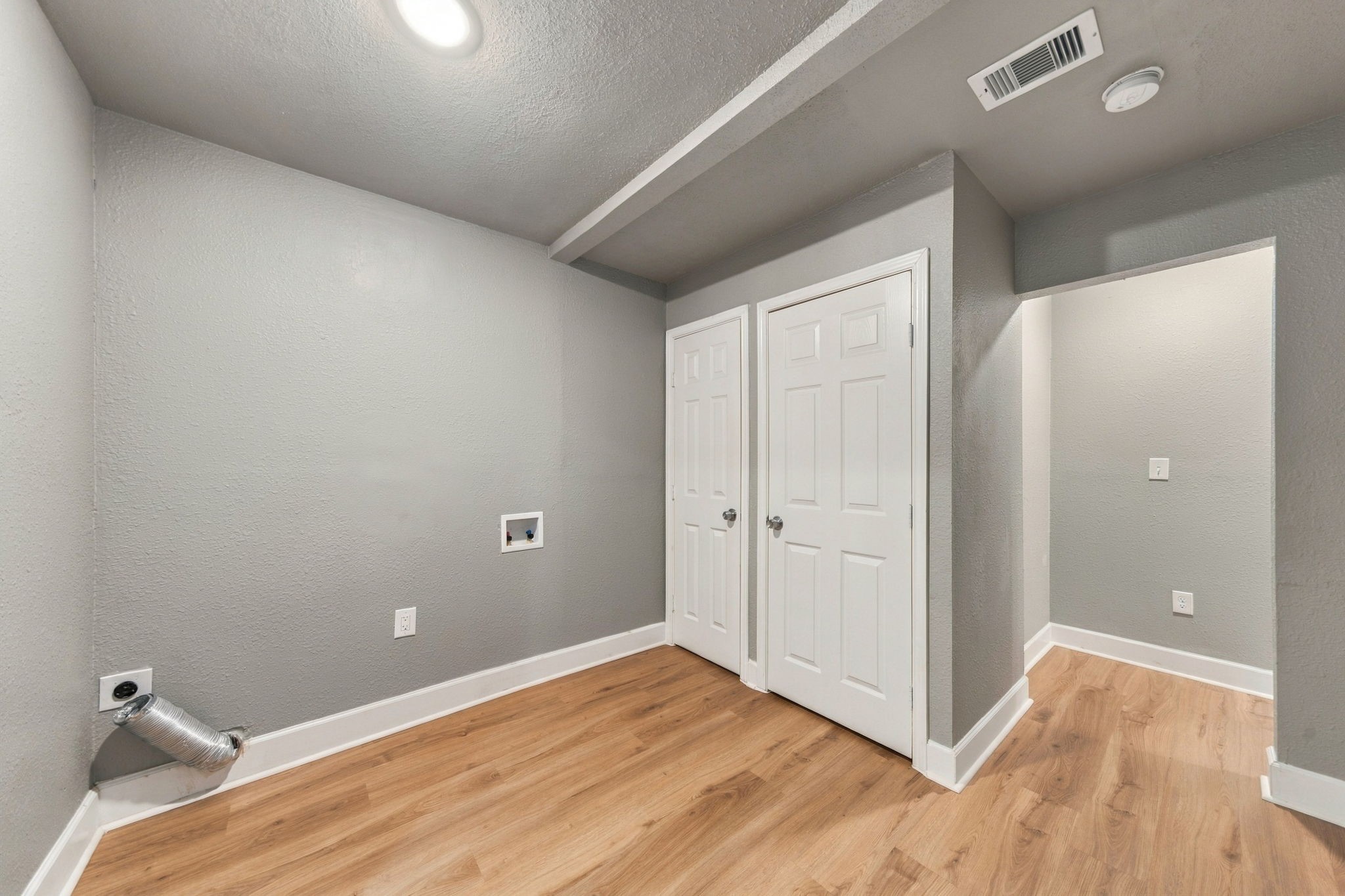Laundry room with modern gray walls, wood flooring, and ample storage space behind dual doors.