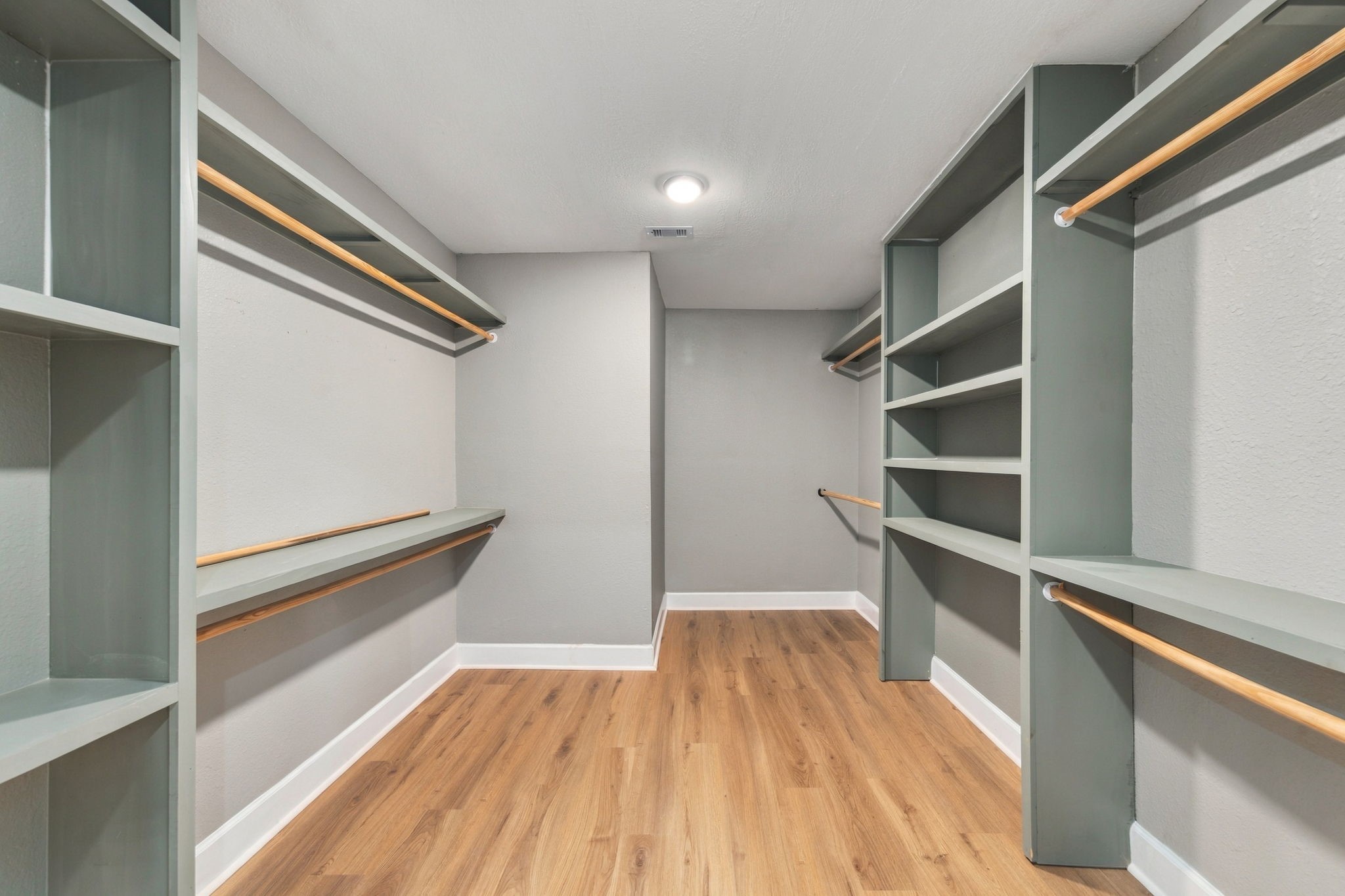 Spacious walk-in closet featuring ample shelving and hanging space, complemented by elegant wood flooring.