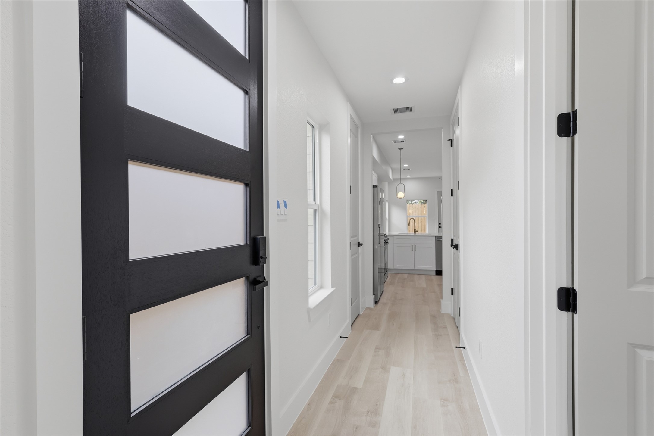 Sleek modern entryway featuring a stylish black door and bright, inviting hallway leading to an open kitchen with contemporary fixtures.