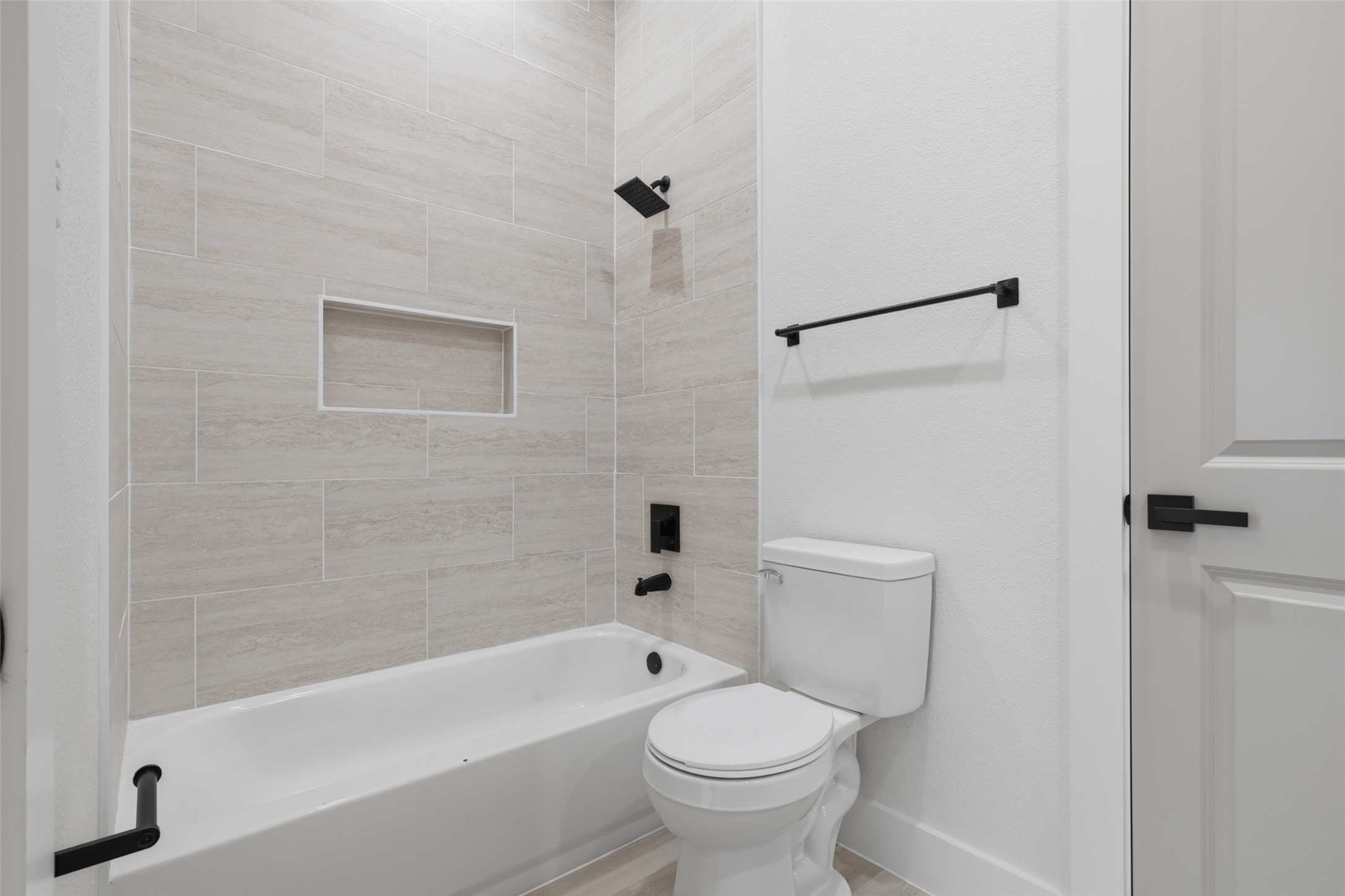 Modern bathroom featuring a sleek bathtub with beige tile surround, a convenient built-in shelf, and contemporary black fixtures.