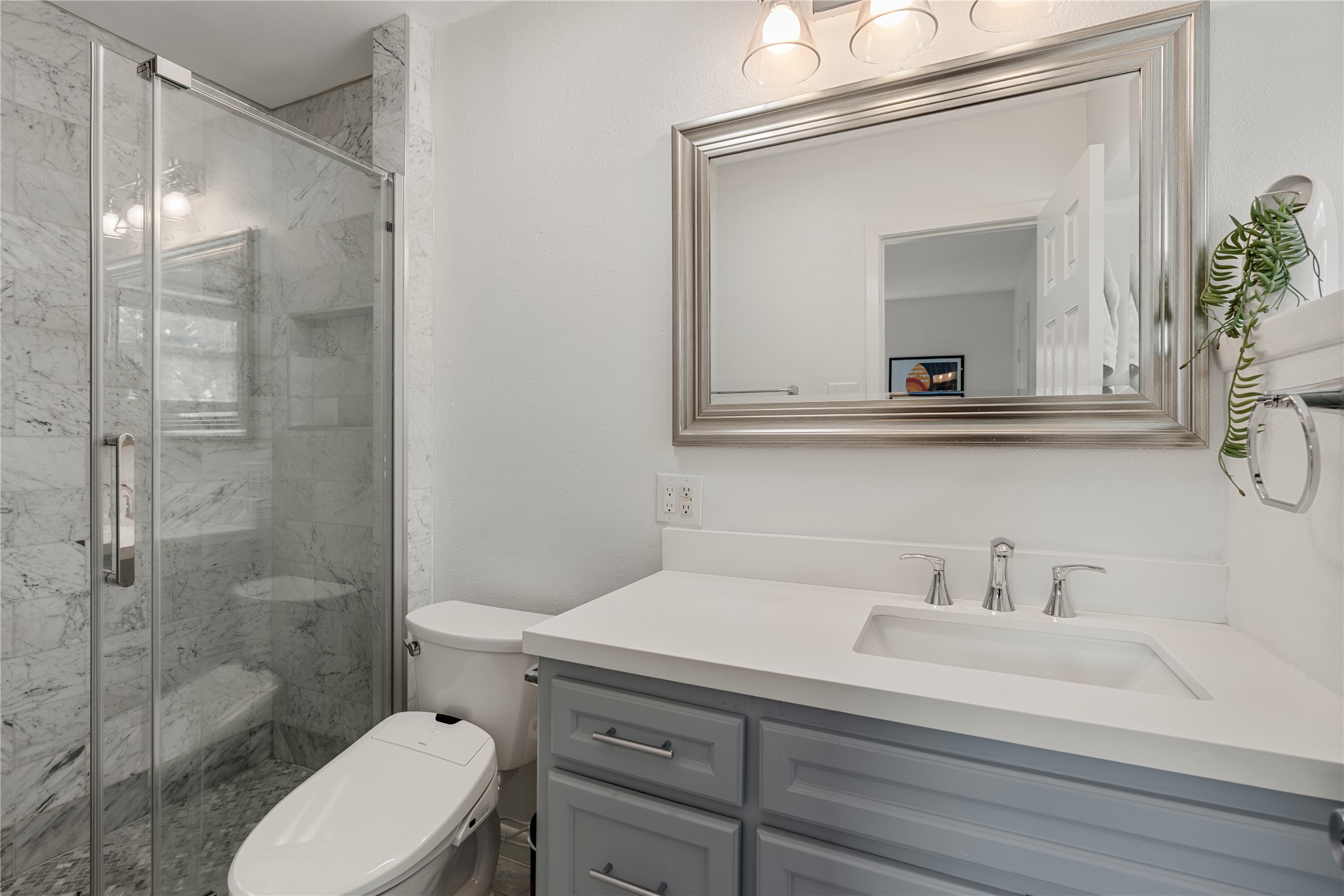 Renovated in 2025, the elegant primary bathroom features a stylish marble-tiled shower, modern fixtures, and a spacious vanity.