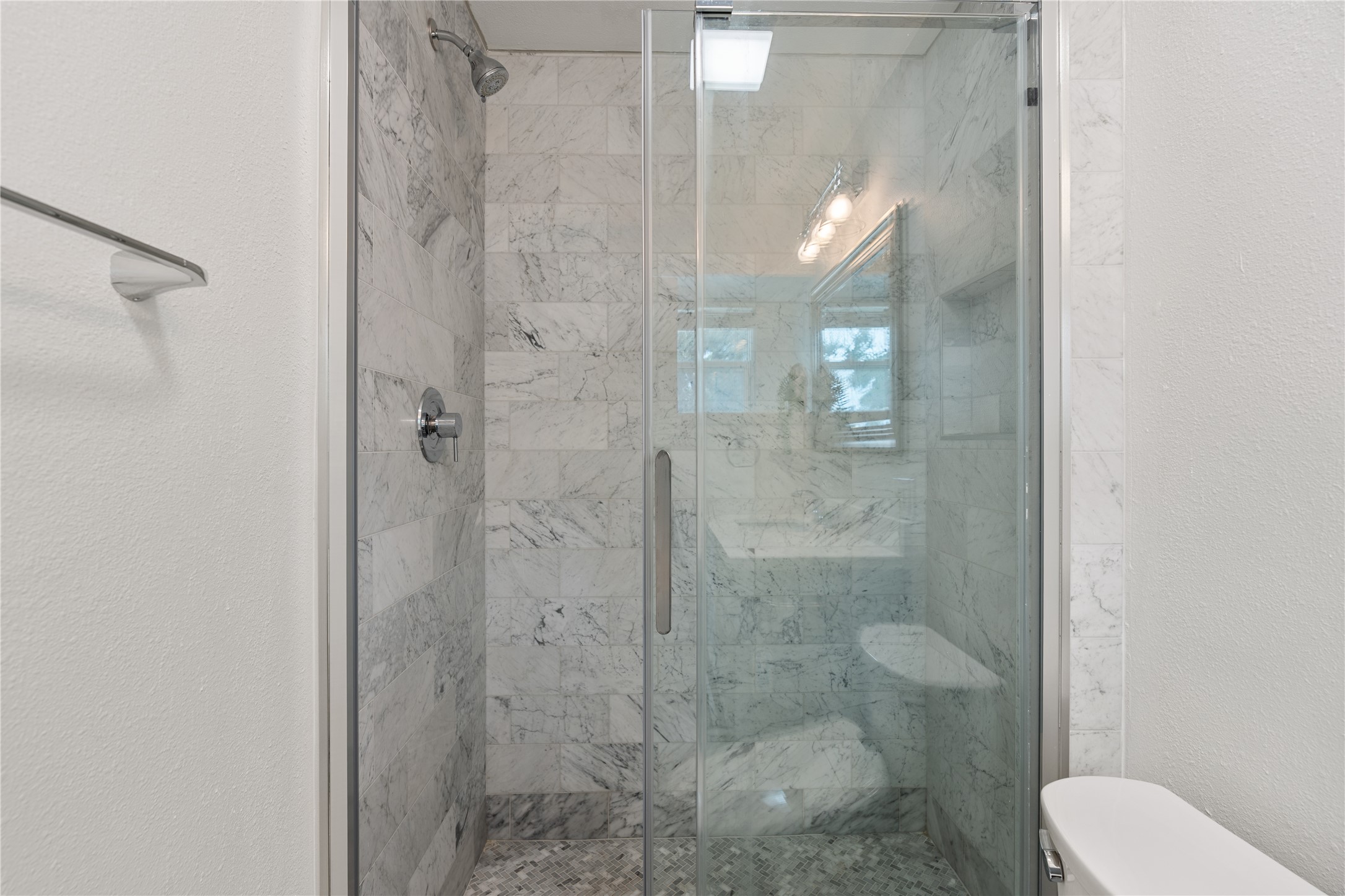Another view of the walk-in shower with beautiful marble style tile with modern fixtures, stainless shower door, and tiled niche.