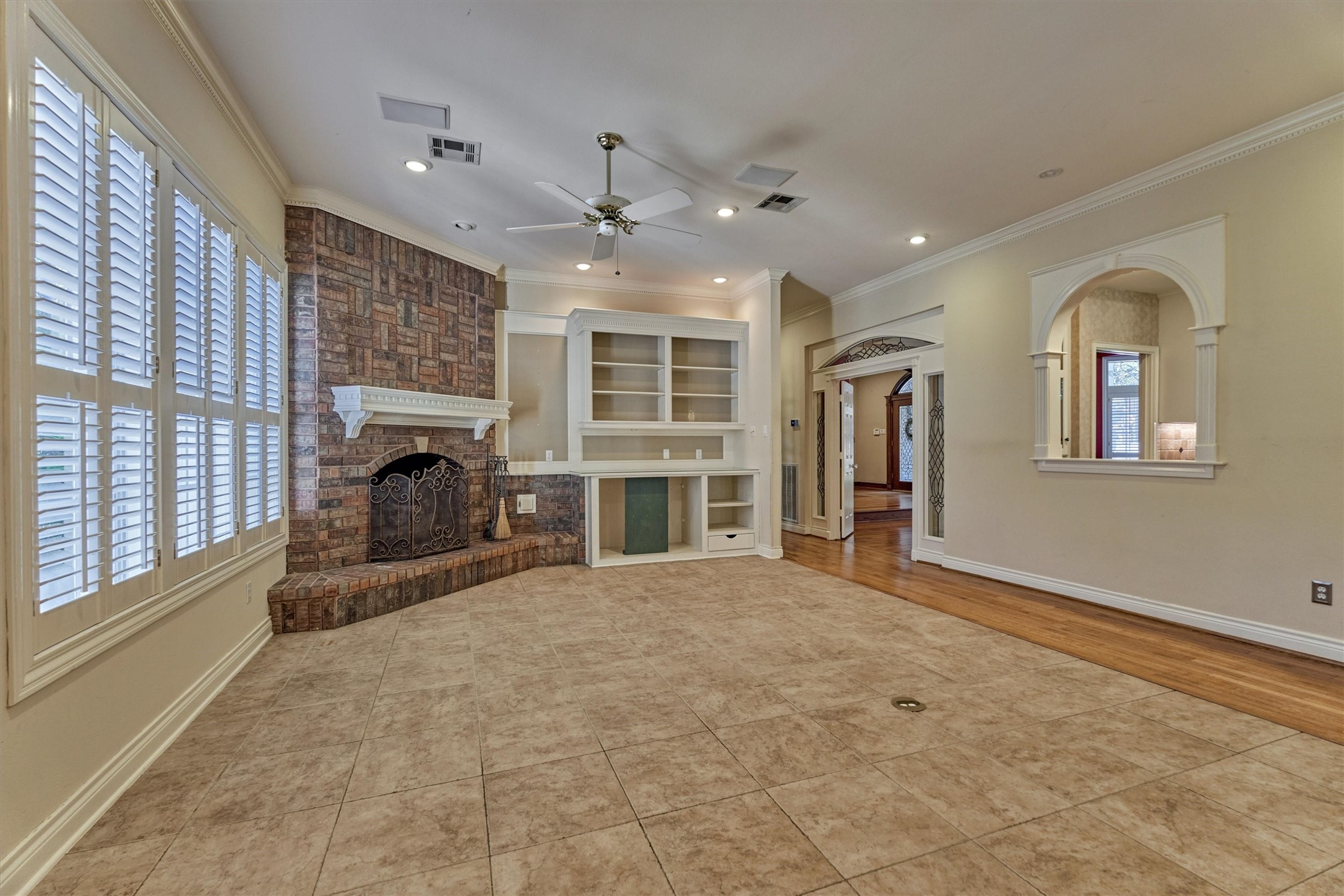 Gather around the gas log fireplace in this downstairs family room, open to the kitchen through an arched pass-through. Large shuttered windows overlook the backyard and fill the room with light. Built-in shelves and cabinets give you room for a TV, books, and dcor, and the mix of tile and hardwood floors is easy to live in.