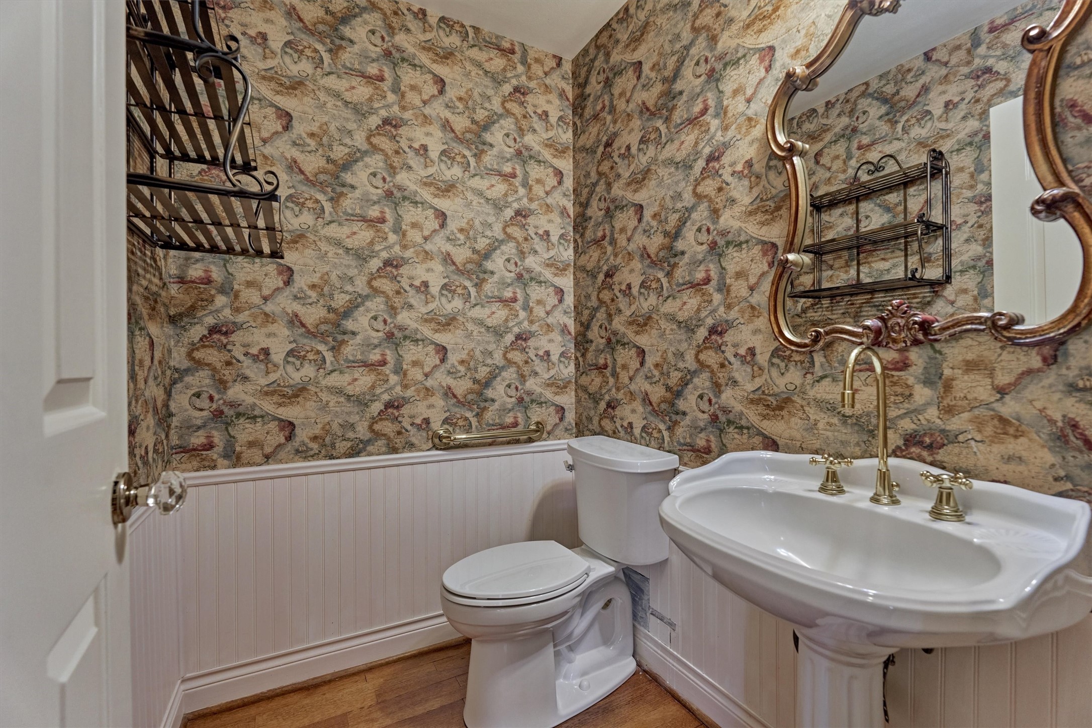 Guests will appreciate this convenient bath, located across from the primary bedroom and open to the office. A pedestal sink with brass fixtures, beadboard wainscoting, and hardwood floors give it a classic, polished look. It works well for visitors and for anyone using the office.