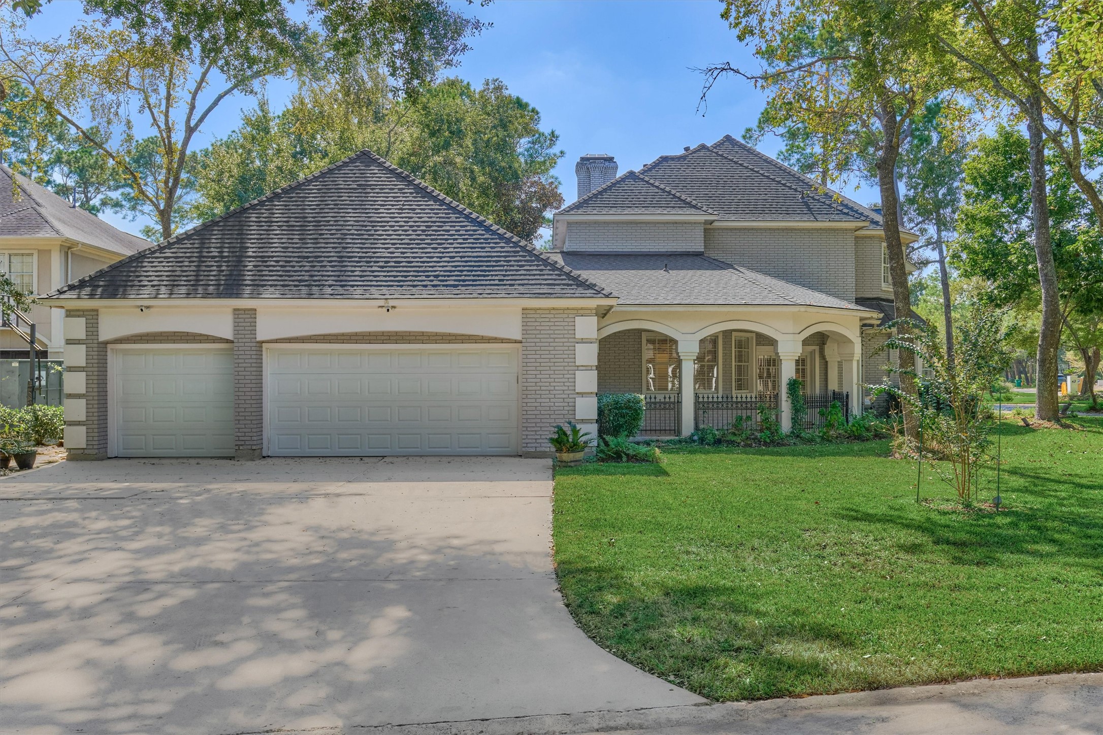 Side view of this corner-lot beauty, featuring a three-car garage with a wide driveway for plenty of parking. The arched, covered front patio is a welcoming spot for morning coffee or evening relaxation, all surrounded by a lush lawn and mature trees.