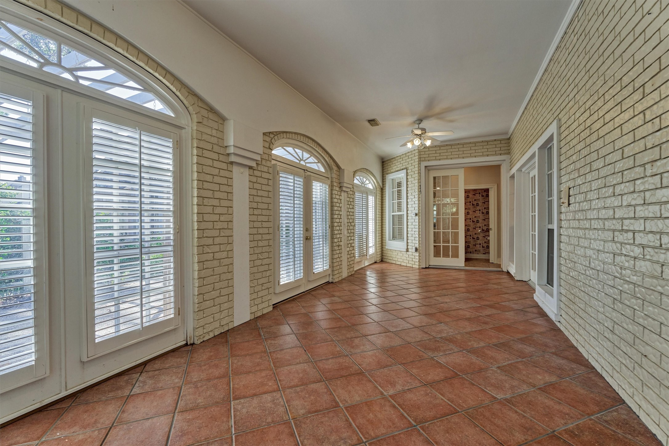 Another angle of the sunroom shows how much natural light this long, flexible space gets. Arched windows and shuttered French doors line the curved wall and look out to the backyard, and the tile floors are easy to maintain. Use it as a game room, sitting area, or hobby space, with direct access to the secondary downstairs suite at the far end. Large closet holds a wine refrigerator.