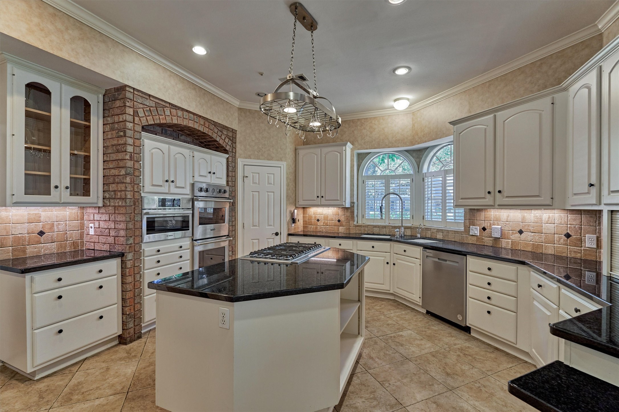 Another angle of this chefs kitchen highlights its bright, open layout. Under-cabinet lighting warms the granite countertops, and a shuttered window over the sink brings in views of the front yard. A walk-in pantry keeps everything organized, and the large island is perfect for prep, serving, or casual meals.
