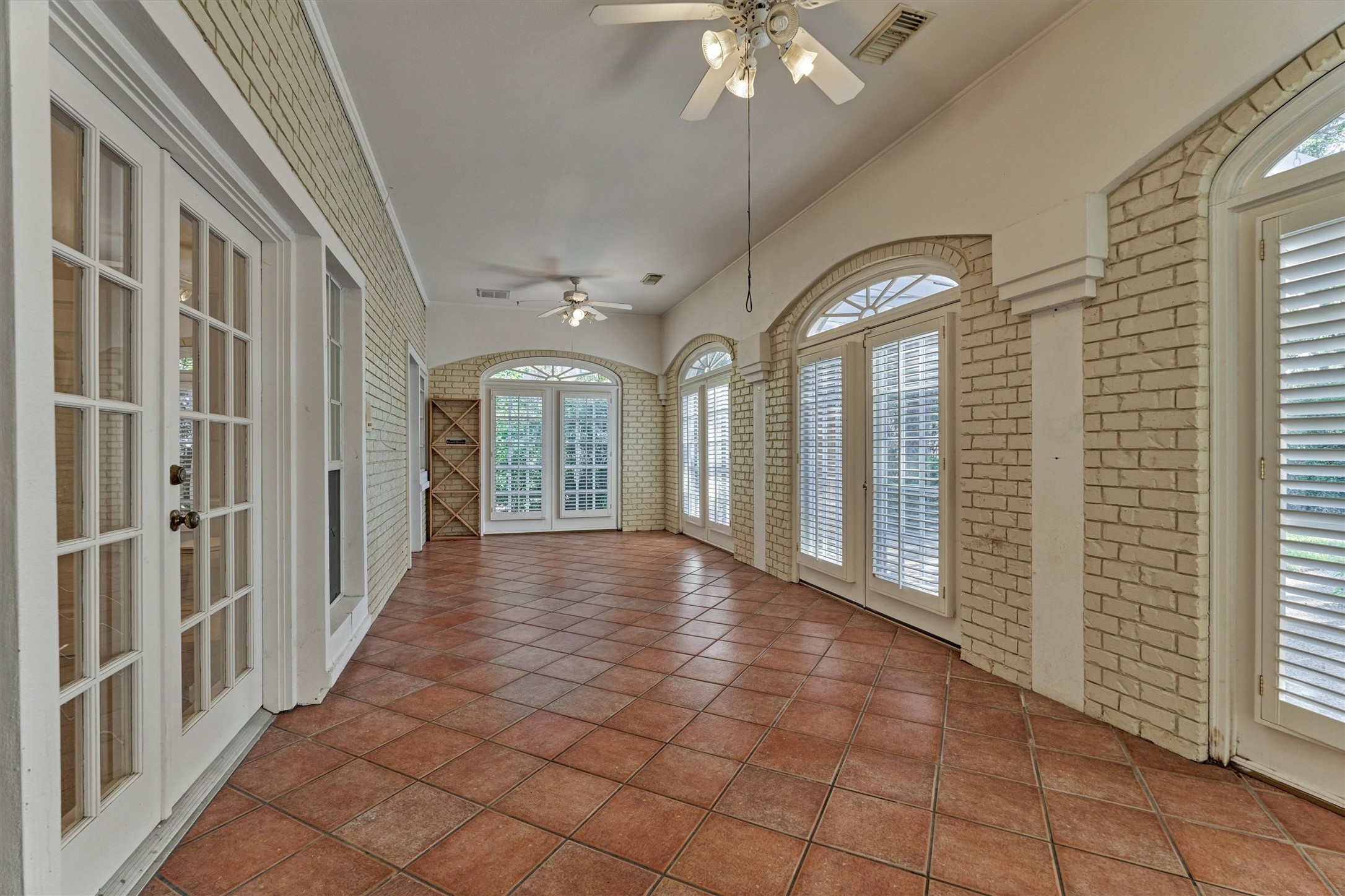 This enclosed sunroom, off the family room, is lined with painted brick walls and arched, transom-topped windows and French doors with plantation shutters. Warm terracotta tile floors are set on the diagonal, and a vaulted, curved ceiling with ceiling fans adds an airy feel. Two sets of double doors give easy access: one opens to the backyard, and the other leads to the secondary downstairs suite.