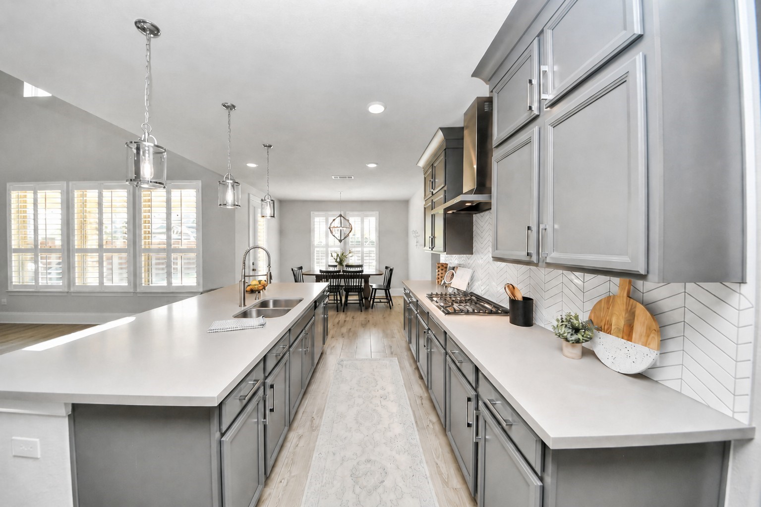 Sleek kitchen with modern gray cabinetry, stainless steel appliances, and a spacious island, leading to a bright dining area with large windows.