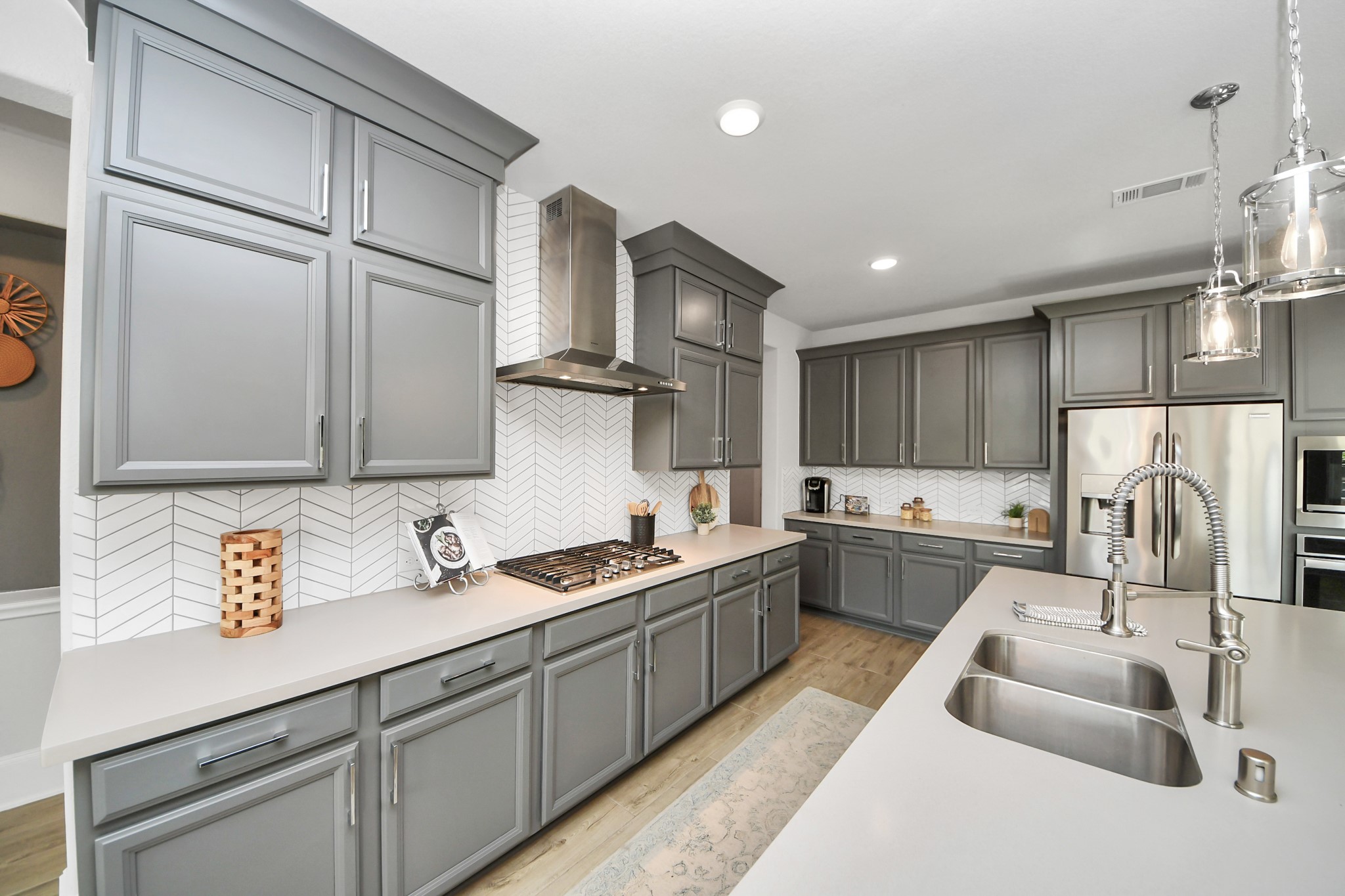 Modern kitchen featuring a stylish herringbone backsplash, and stainless-steel appliances, complemented by a spacious island with chic pendant lighting.