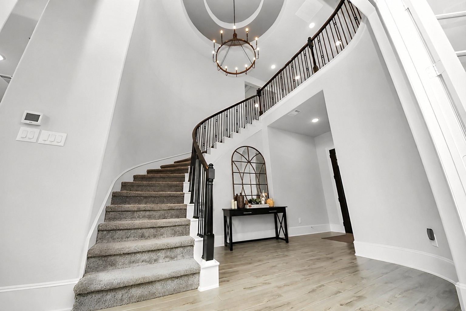Elegant entryway featuring a grand curved staircase, complemented by a stylish chandelier and sleek wood look tile flooring.