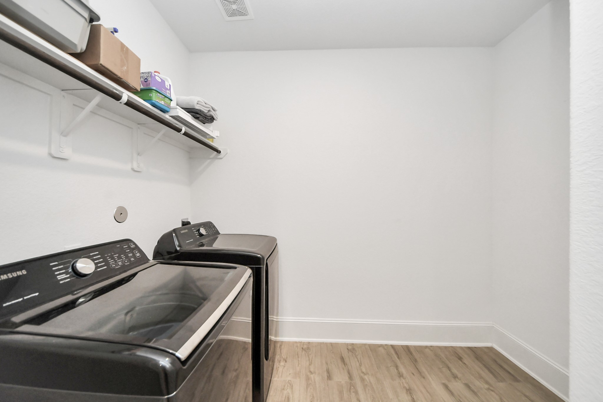 Spacious laundry room with shelving, and sleek wood look tile flooring. Oversized and recently purchased washer and dryer are available for purchase.