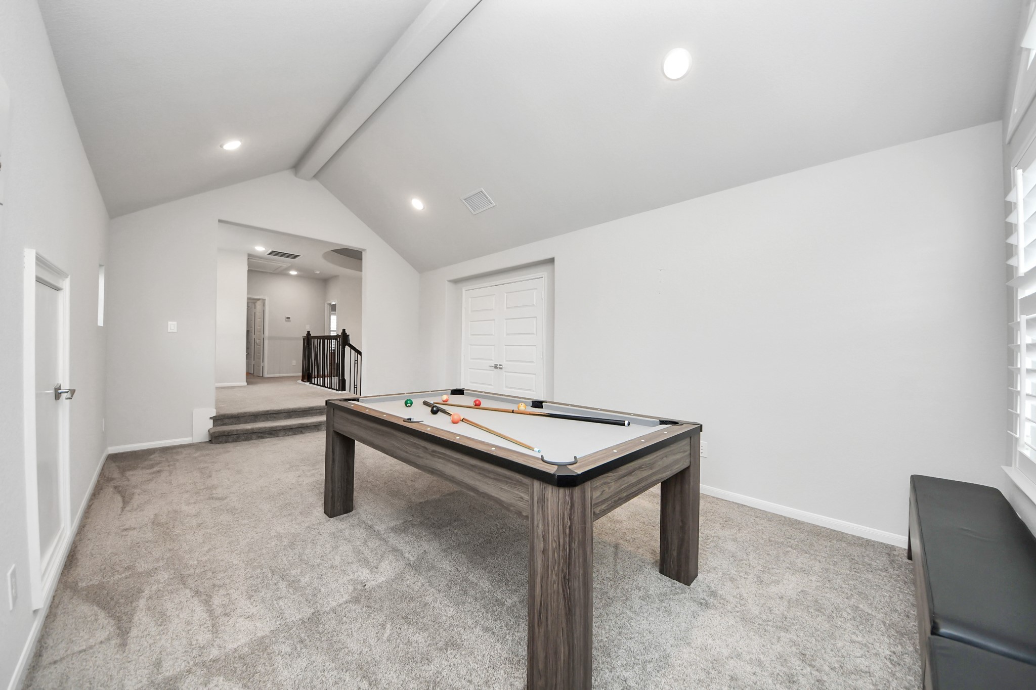 An upstairs game room with cathedral ceilings. The media room doors are to the right and a fully decked out additional attic space is to the left. The pool table which converts to a ping pong table, or gaming table with bench seats can be purchased separately if desired.