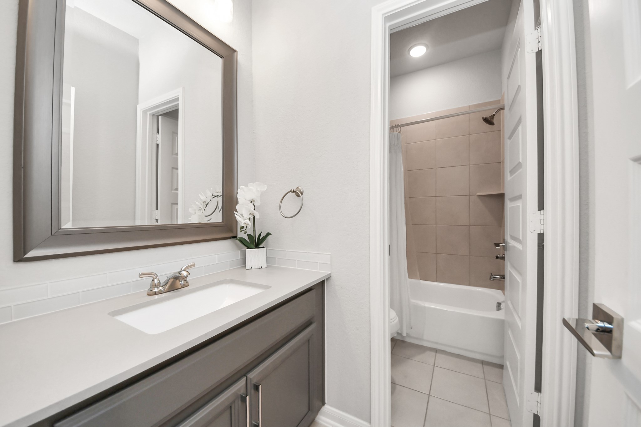 This secondary bathroom also contains a sleek vanity, with updated light fixture, large, framed mirror, and a tiled shower-tub combo for a functional and stylish space. It is found right next to the previous secondary bedroom picture.