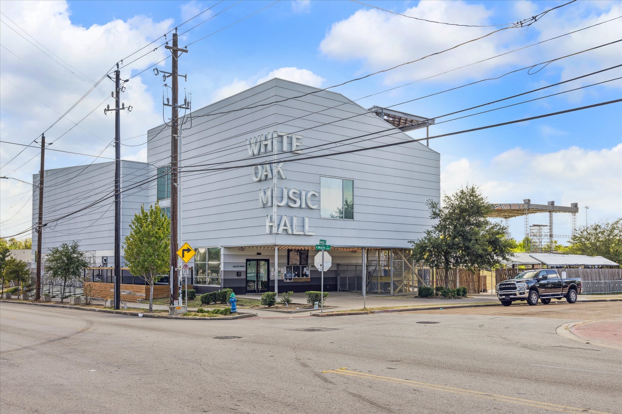 Modern music hall with sleek architecture and prominent signage, located on a bustling street corner nearby.