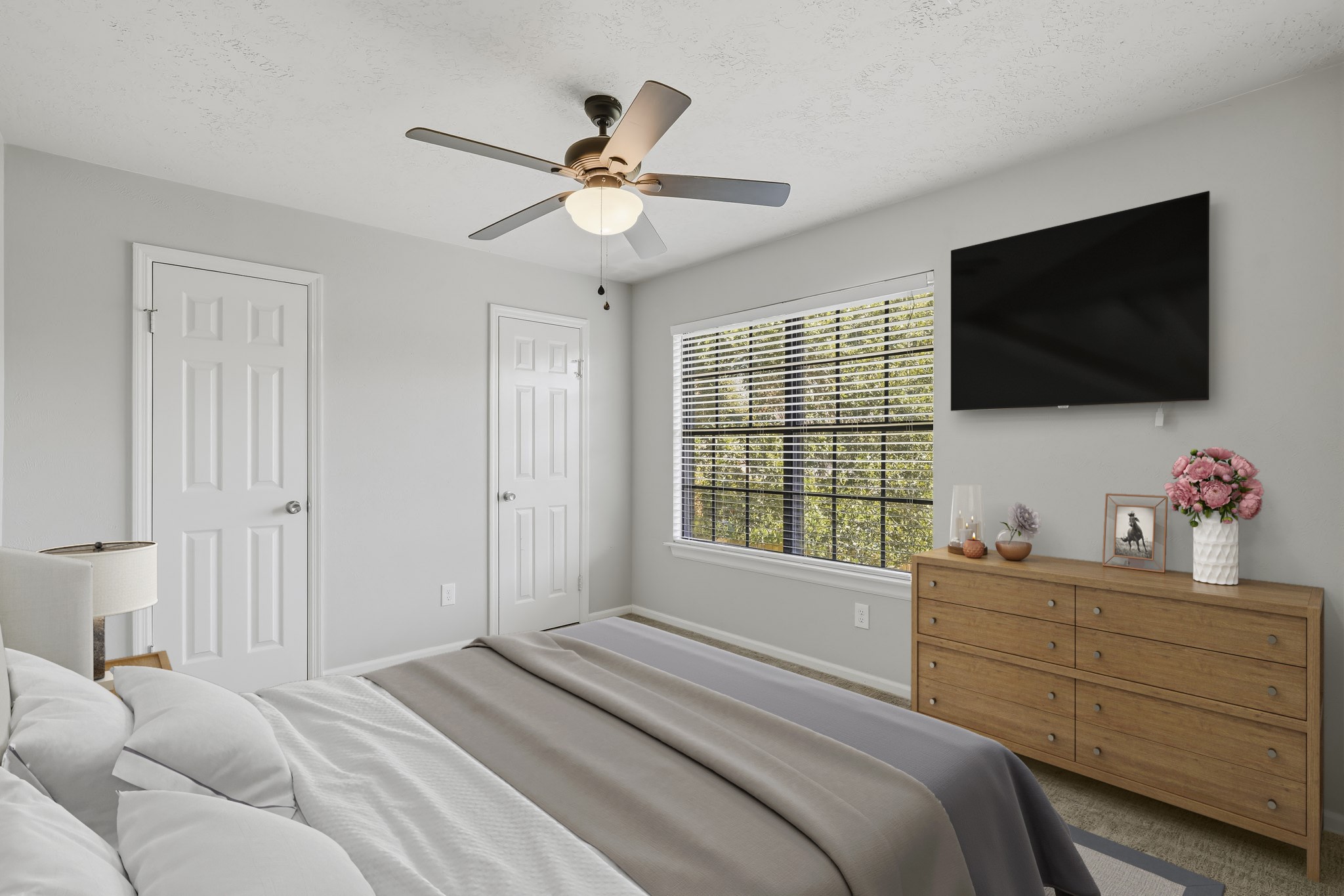 Virtually Staged: This inviting secondary bedroom features neutral gray walls, soft carpeting, and a large window that brings in plenty of natural light. A ceiling fan adds everyday comfort, while the spacious layout, closet storage, and versatile floor plan provide plenty of room for a complete bedroom setup.