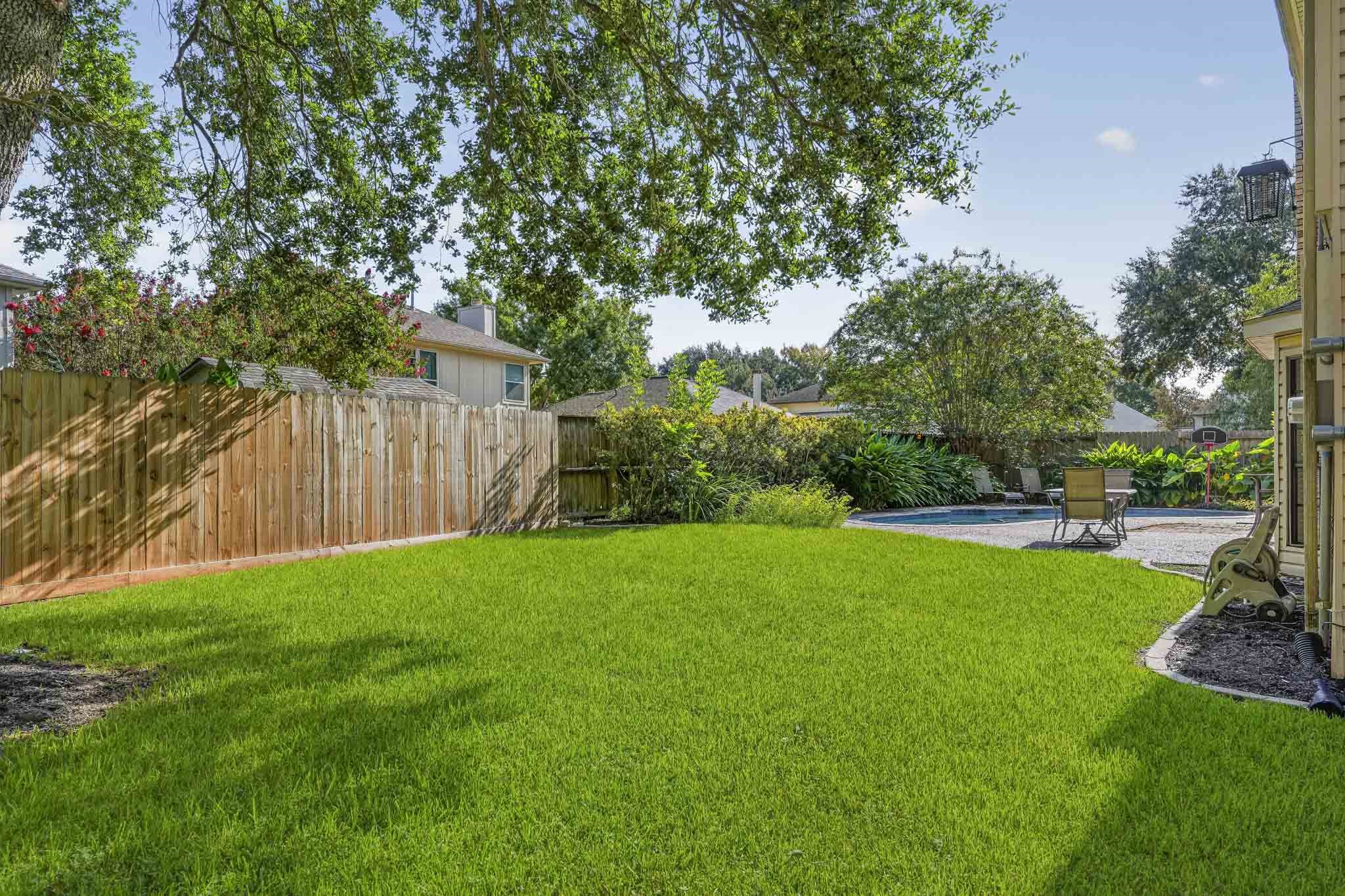 The fenced backyard is framed by mature trees and lush landscaping.