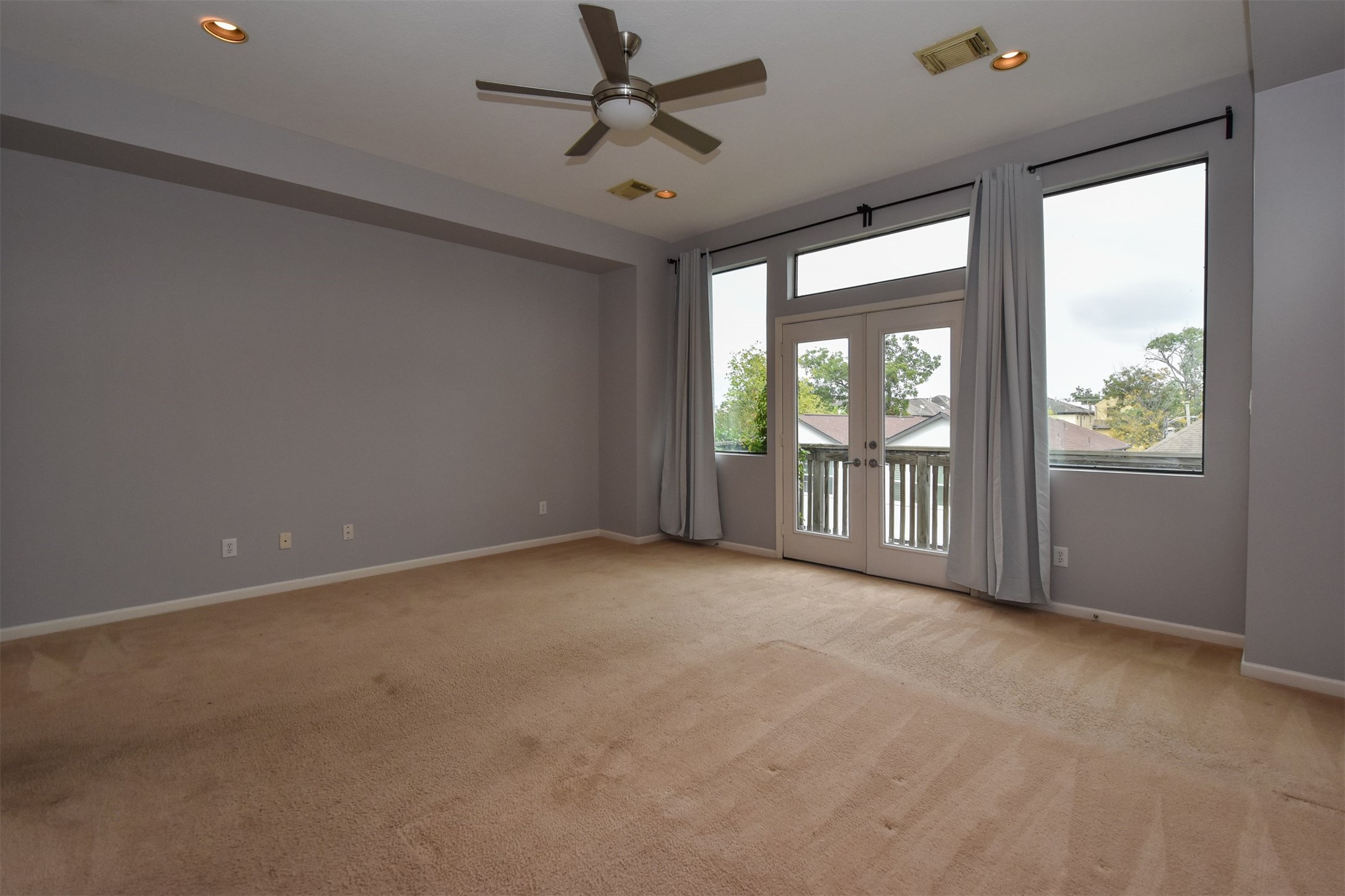 Spacious master bedroom with french doors leading to balcony, recessed lighting & ceiling fan