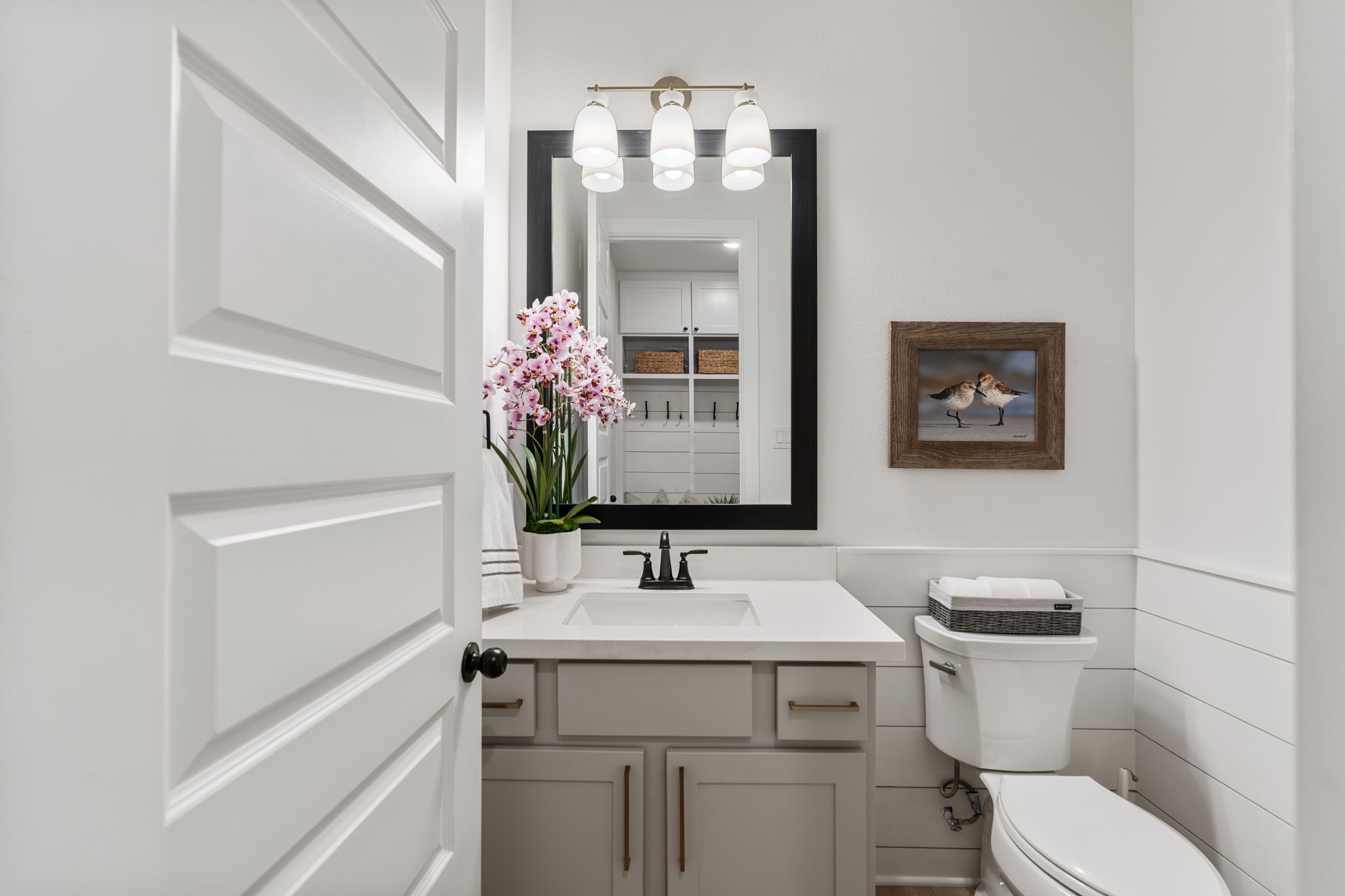 Beautifully appointed powder bath featuring elegant shiplap accents, designer lighting, a framed mirror, stylish vanity, and sophisticated finishes throughout.