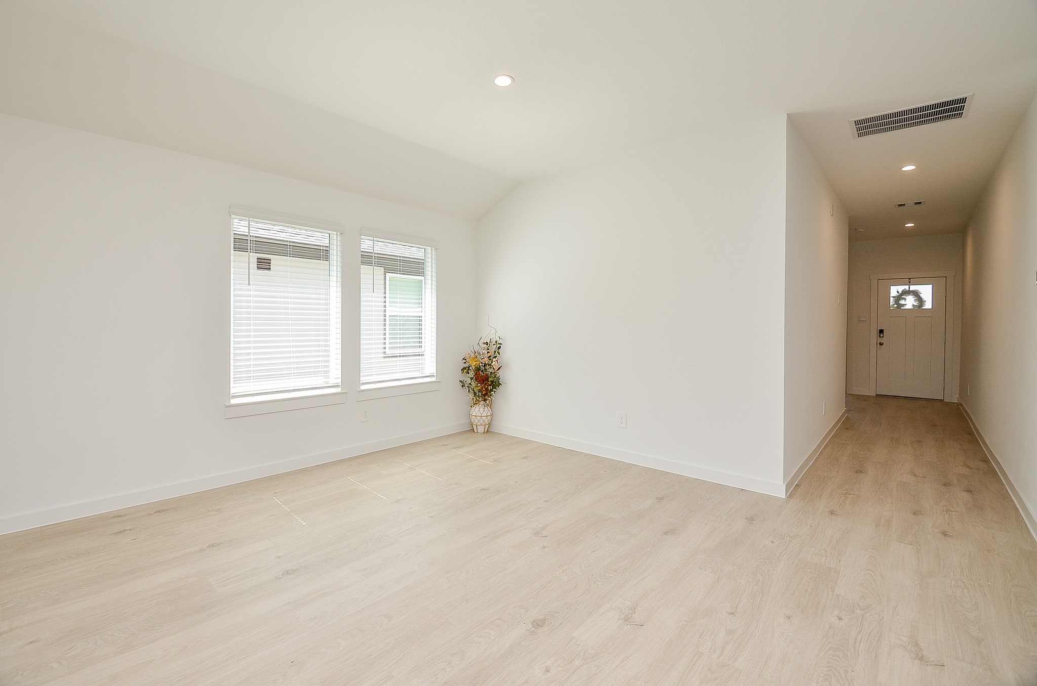 Bright and airy living space featuring sleek wood flooring, ample natural light from large windows, and a welcoming entryway.