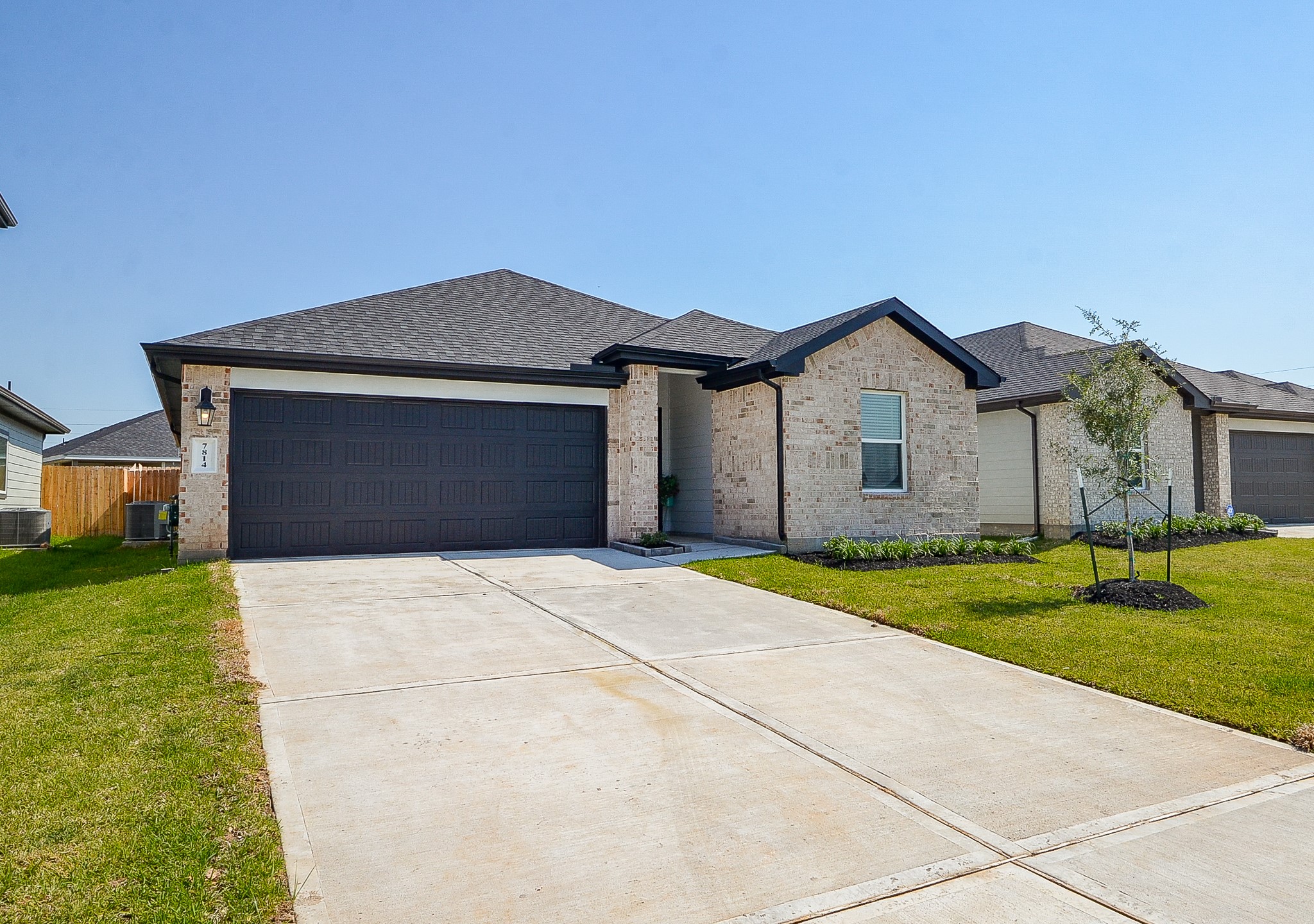 Charming single-story home featuring a modern brick exterior, sleek dark garage door, and a spacious driveway, set on a beautifully manicured lawn.