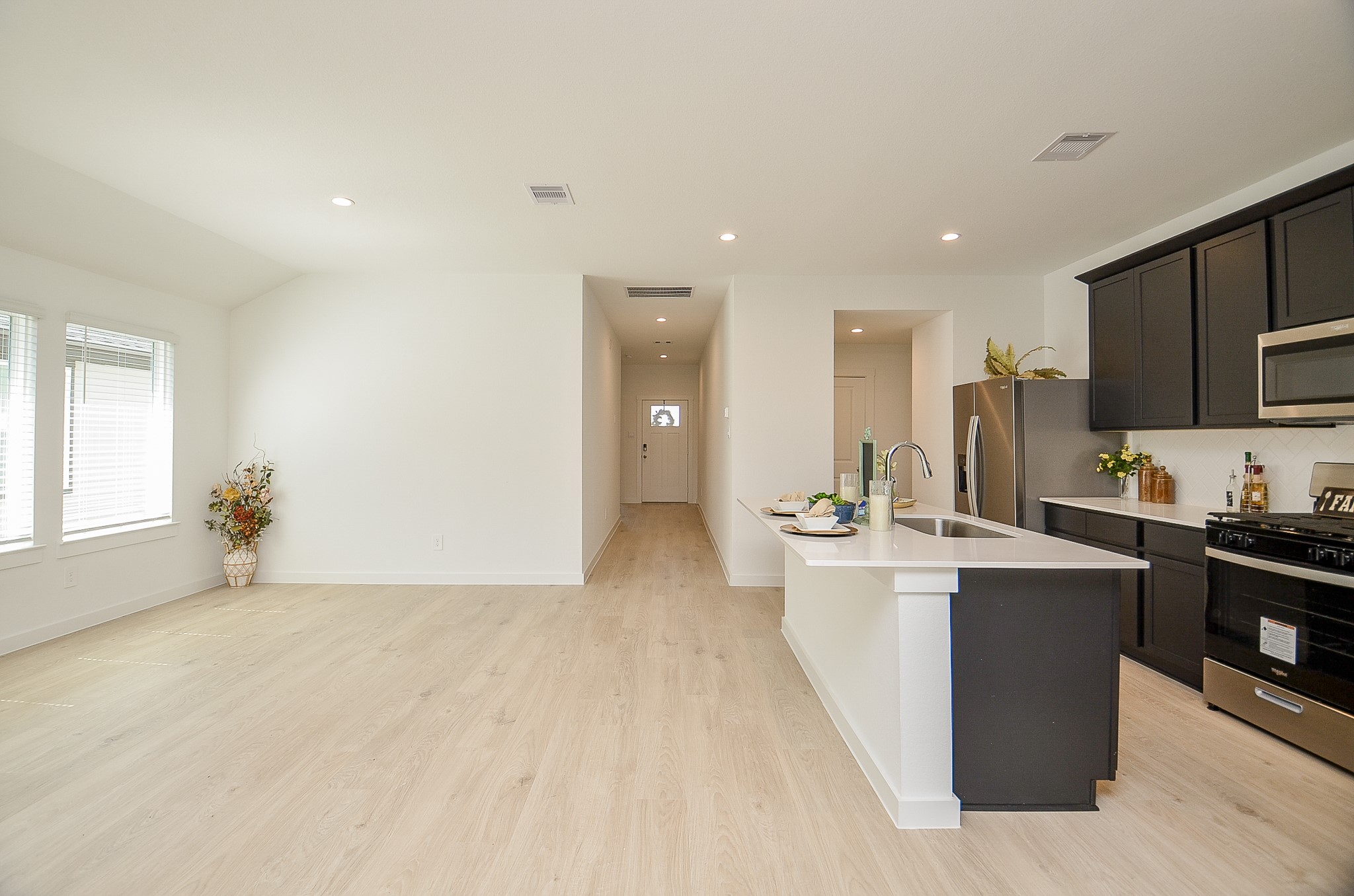 Spacious open-concept kitchen and living area featuring sleek dark cabinetry, modern appliances, and ample natural light from large windows.