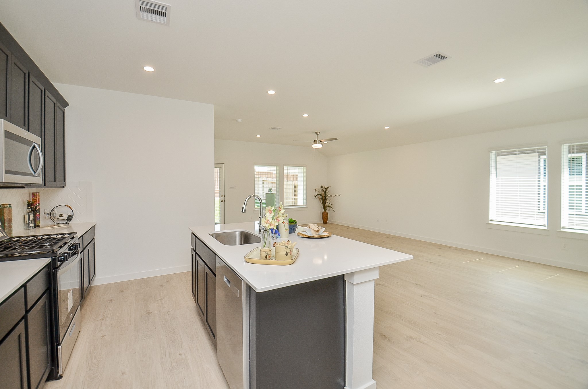 Bright and spacious open-concept kitchen and living area featuring sleek dark cabinetry, modern stainless steel appliances, and a large island with ample seating space.