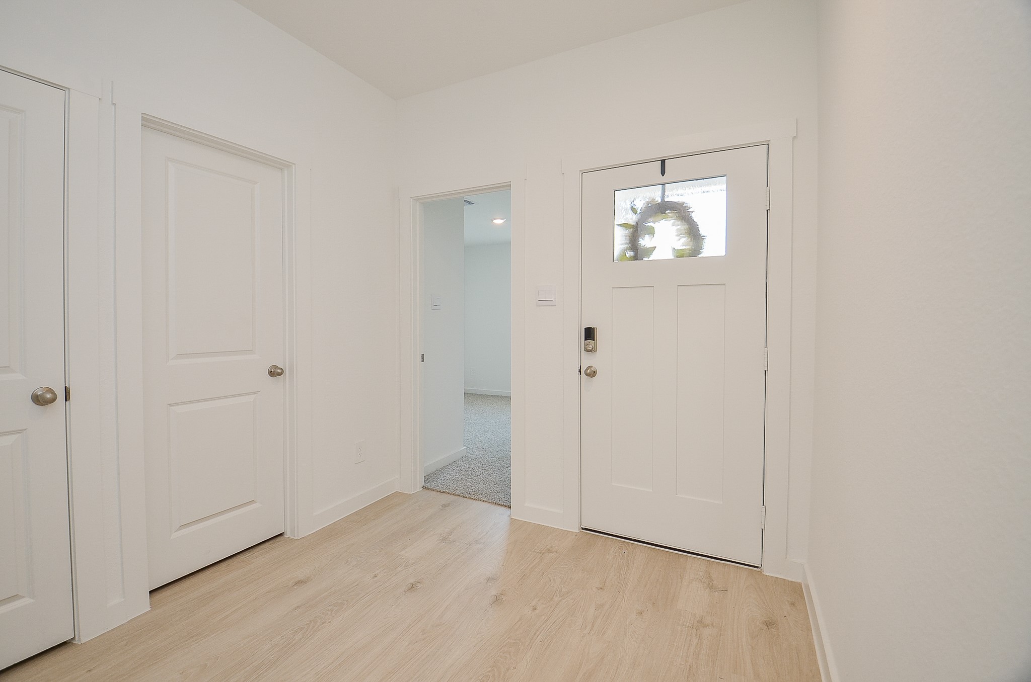 Bright and welcoming entryway featuring modern white doors, sleek hardware, and light wood flooring.