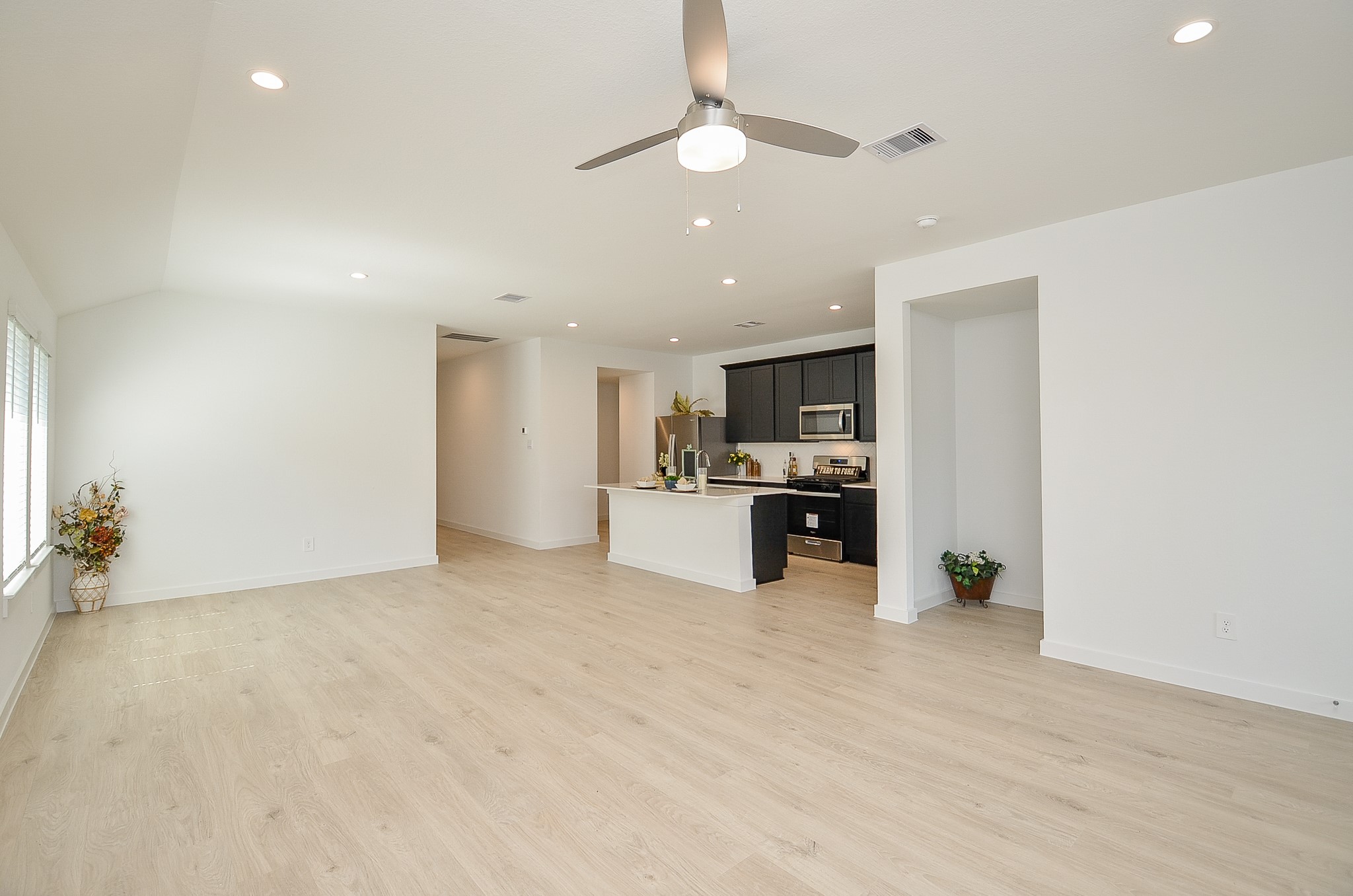 Spacious open-concept living area with modern light wood floors, recessed lighting, and a sleek kitchen featuring dark cabinetry and stainless steel appliances.