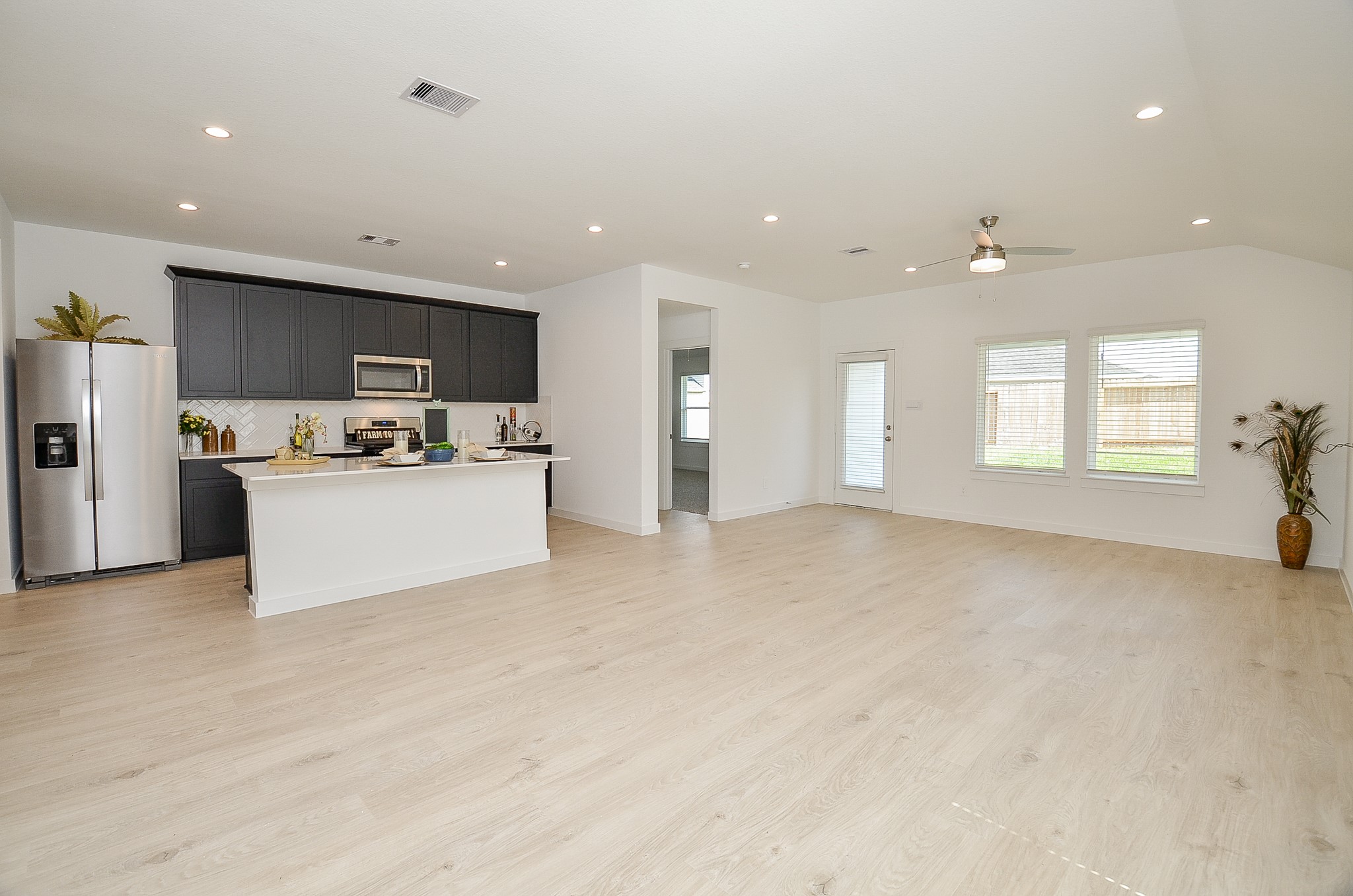 Spacious open-concept living area featuring sleek hardwood floors, a modern kitchen with dark cabinetry and stainless steel appliances, and ample natural light from large windows.