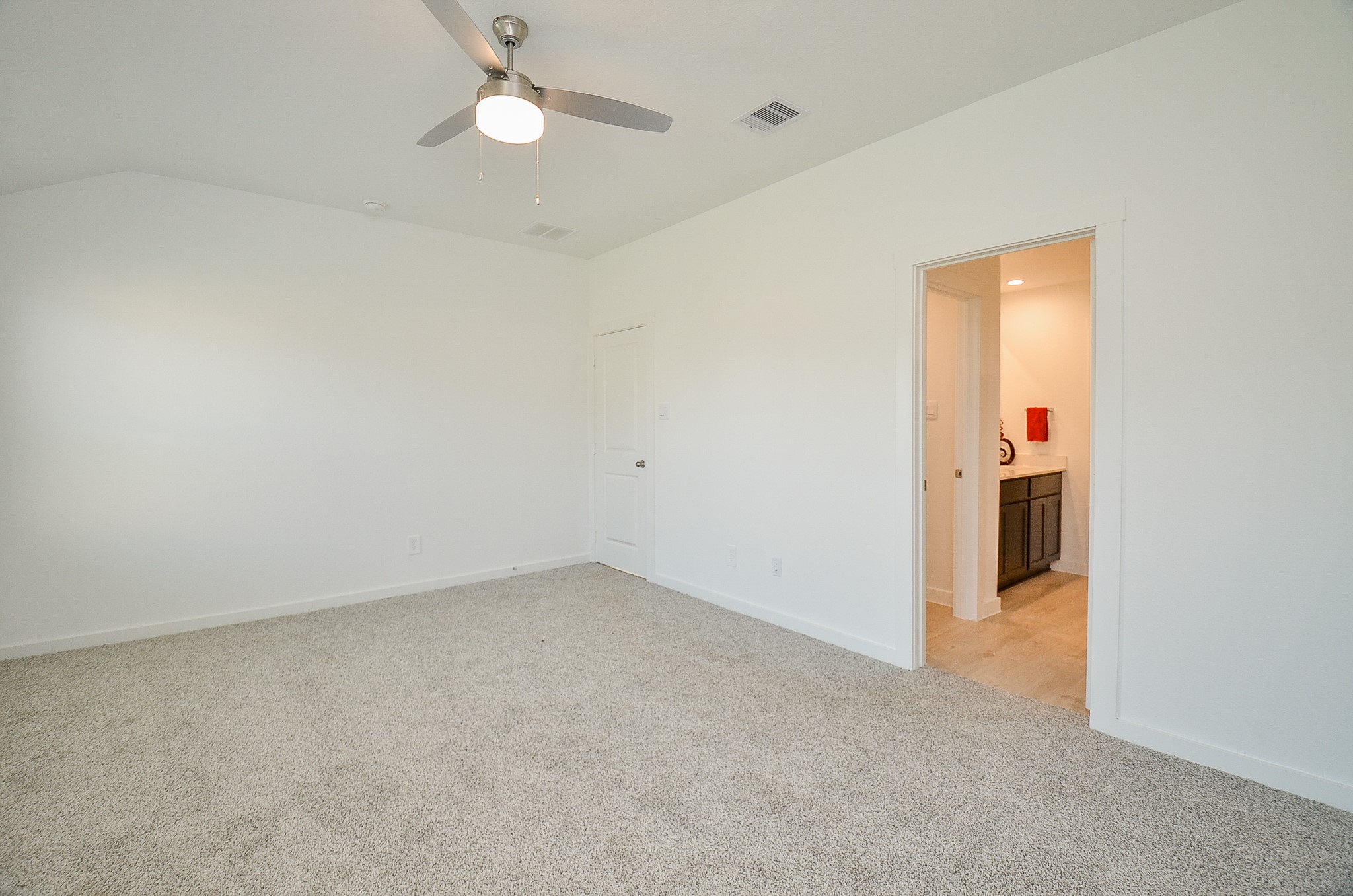 Spacious bedroom with plush carpeting, modern ceiling fan, and an en-suite bathroom for added convenience.