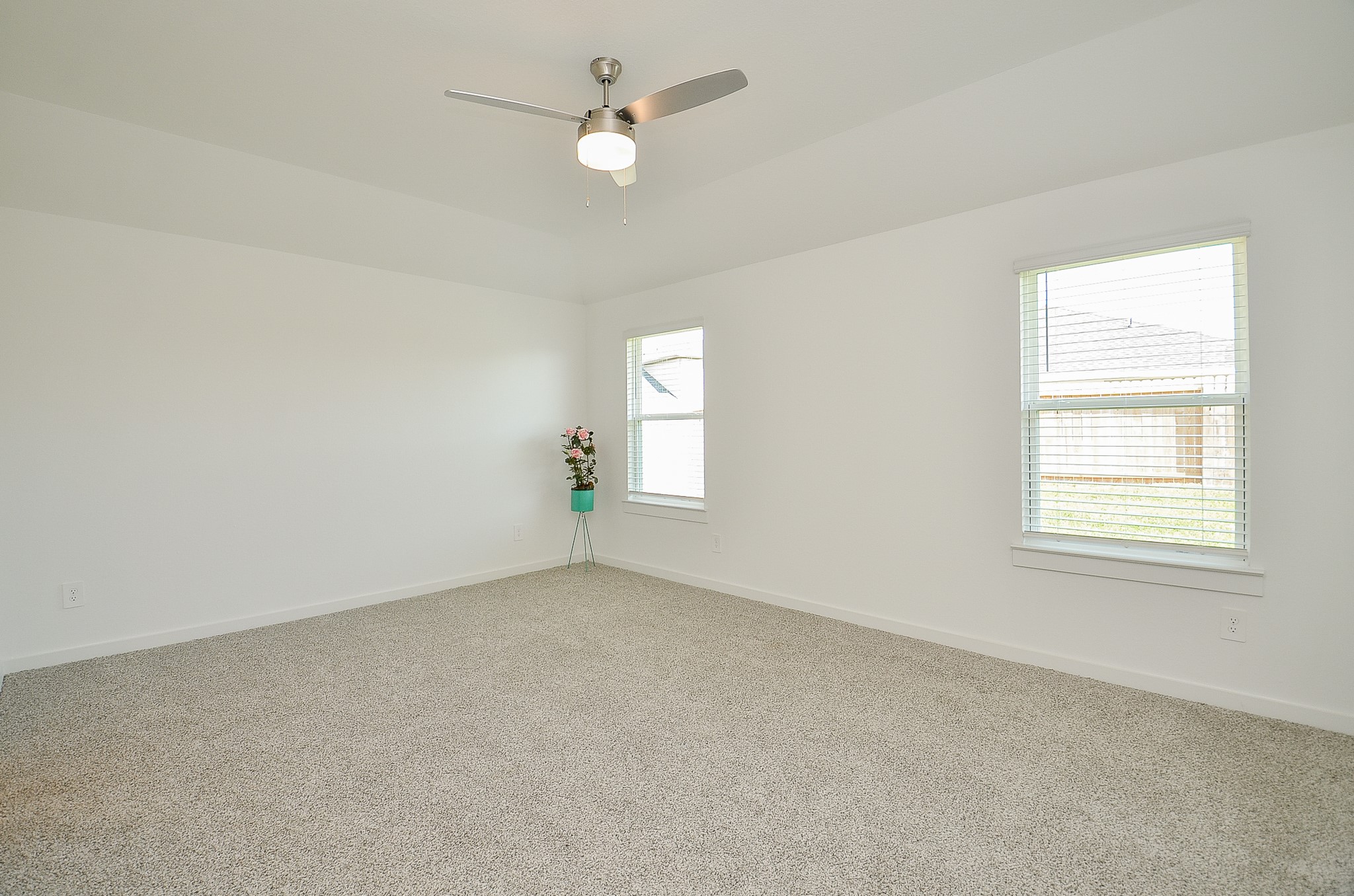 Spacious, light-filled room with neutral carpeting and modern ceiling fan, ideal for a cozy retreat or versatile living space.