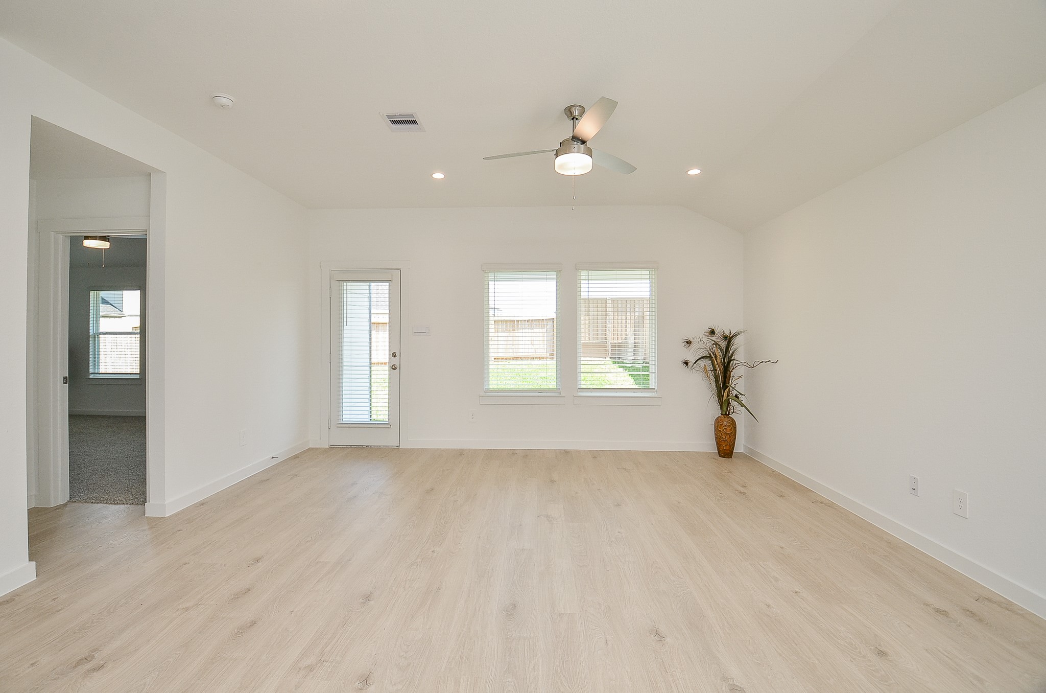 Bright and spacious living area with light wood flooring, large windows, and a ceiling fan, offering ample natural light and a seamless indoor-outdoor flow.