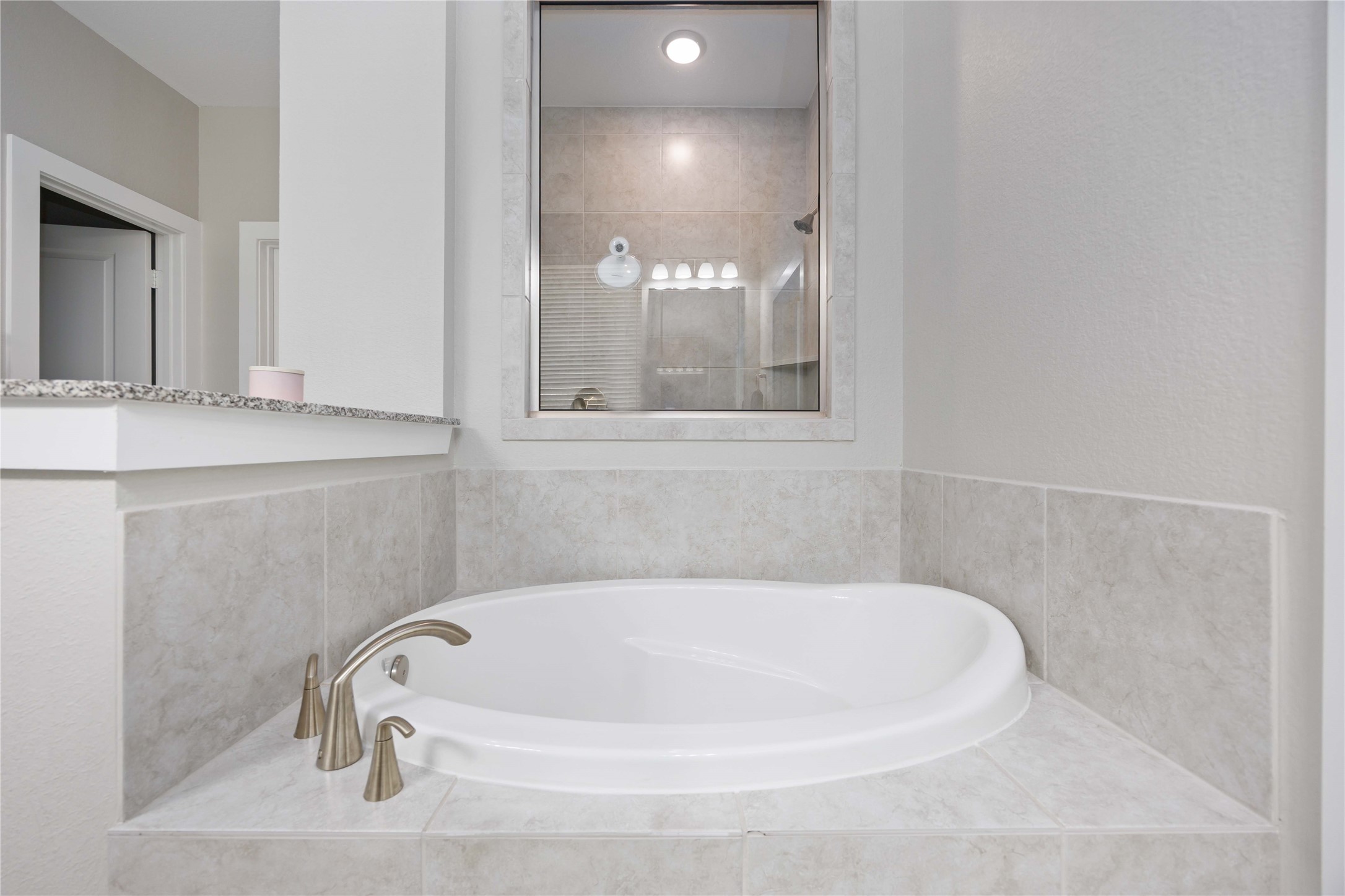This bathroom features a modern, corner oval bathtub with sleek fixtures, surrounded by light beige tiles, creating a clean and elegant look.