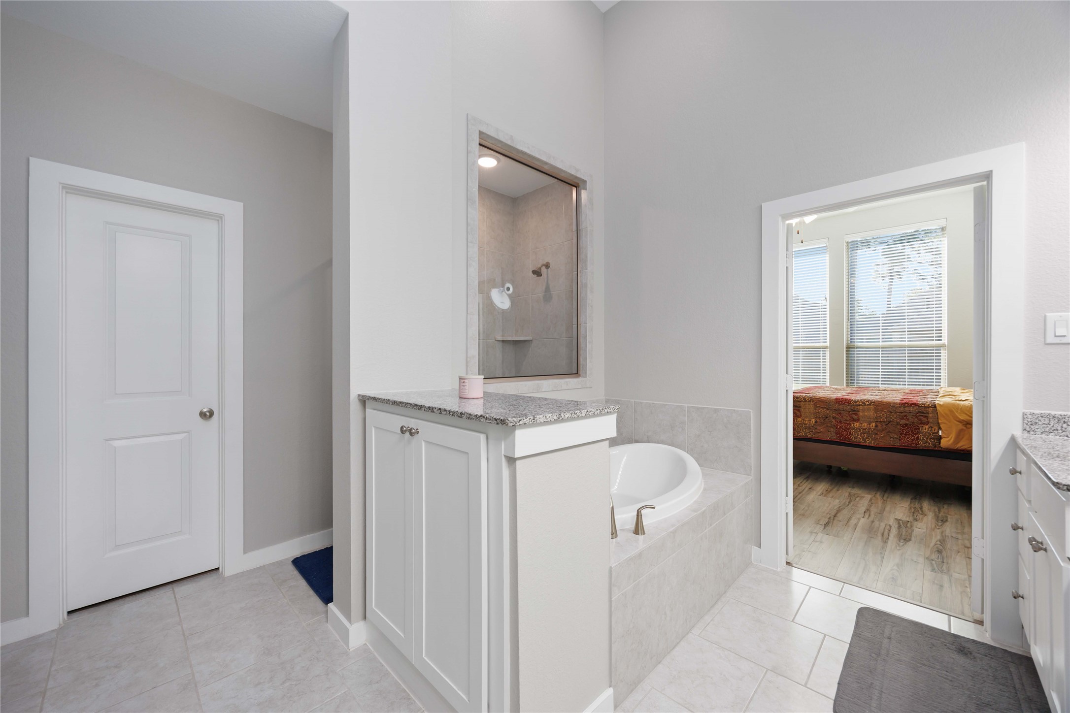This bathroom features a modern design with a corner bathtub, separate shower, and neutral tile flooring. It connects to a bedroom with large windows, offering plenty of natural light.